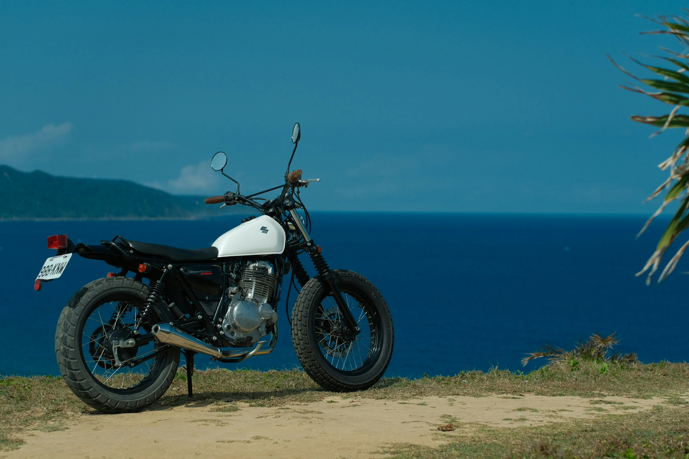 海辺の砂地に停められたスズキのバイク（Suzuki Tu250）