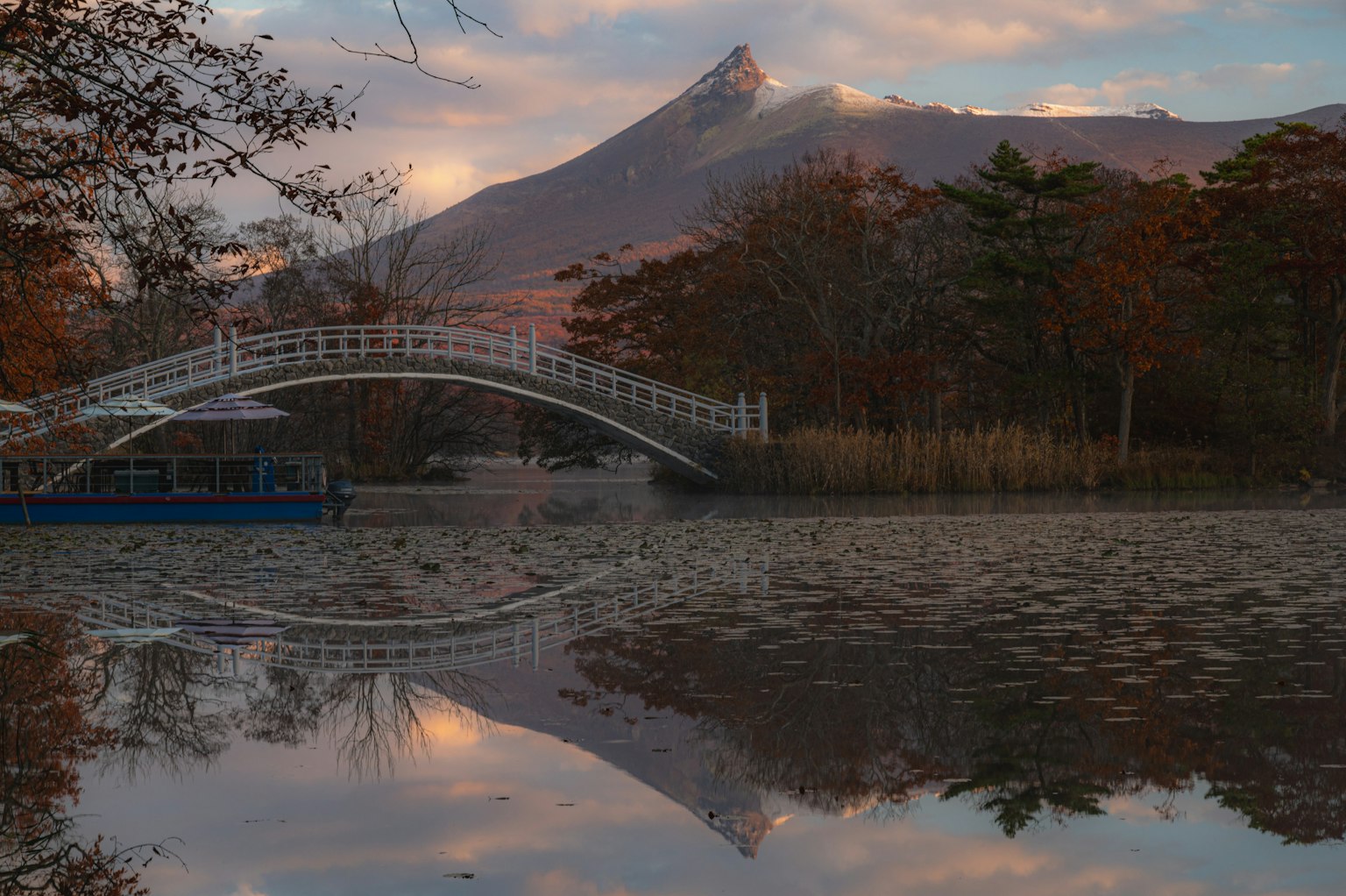 A serene lake reflecting a beautiful bridge and a mountain landscape