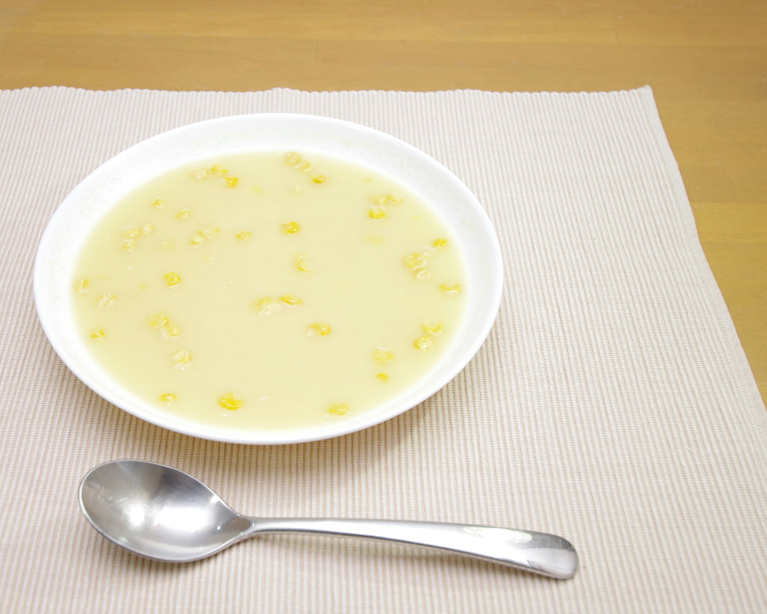 Un bol de soupe de couleur jaune clair sur un sous-plat avec une cuillère à côté