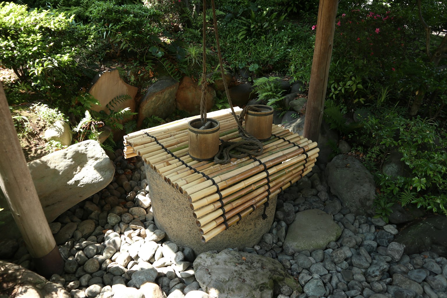 Bambuswasserbecken mit zwei Töpfen auf einer Steinbasis in einem Garten