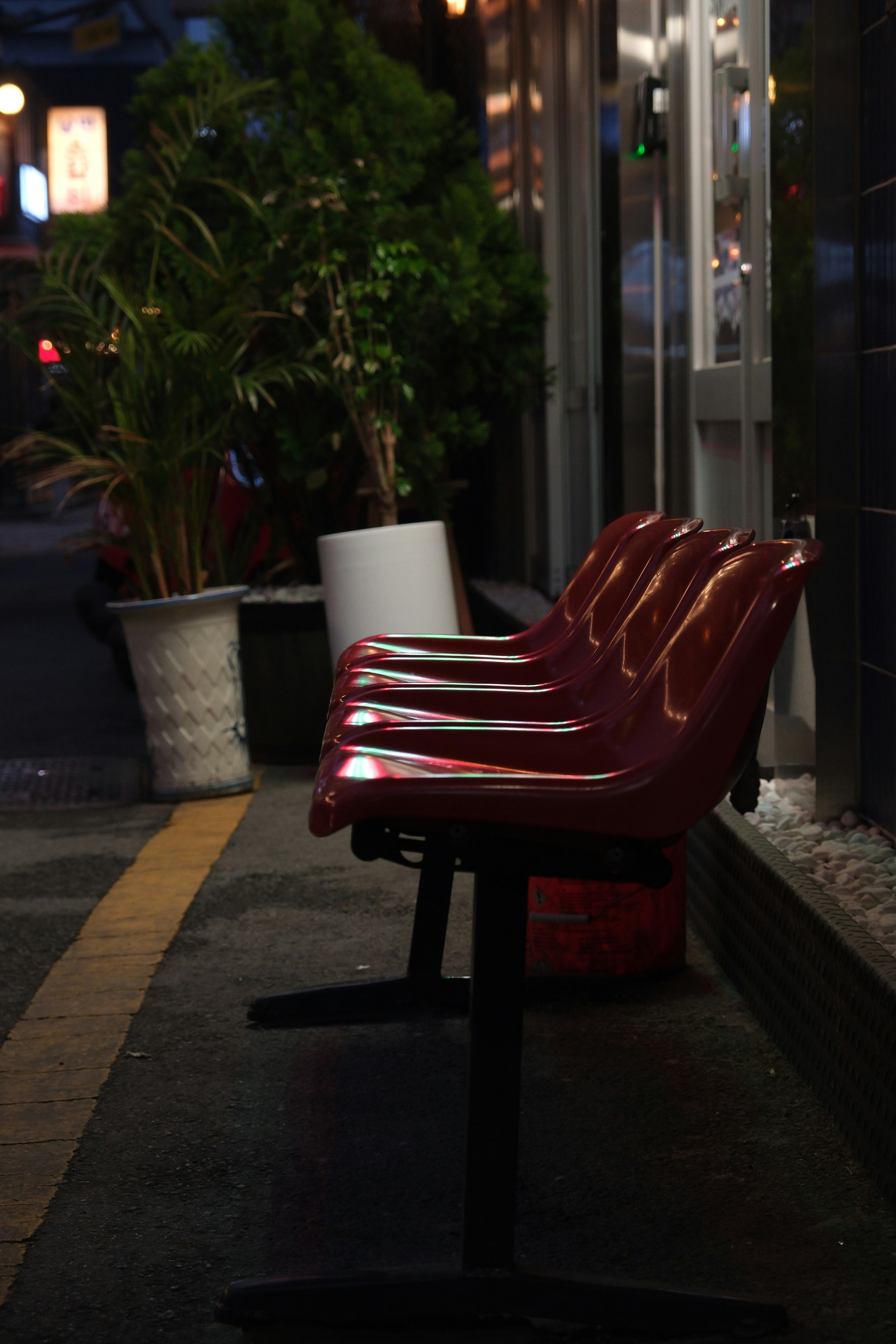 夜の屋外通路に置かれた赤いベンチと鉢植えのある街角