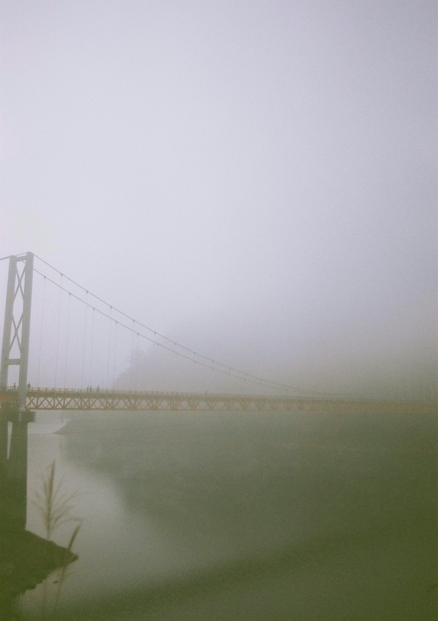 A fog-covered suspension bridge with a serene water surface