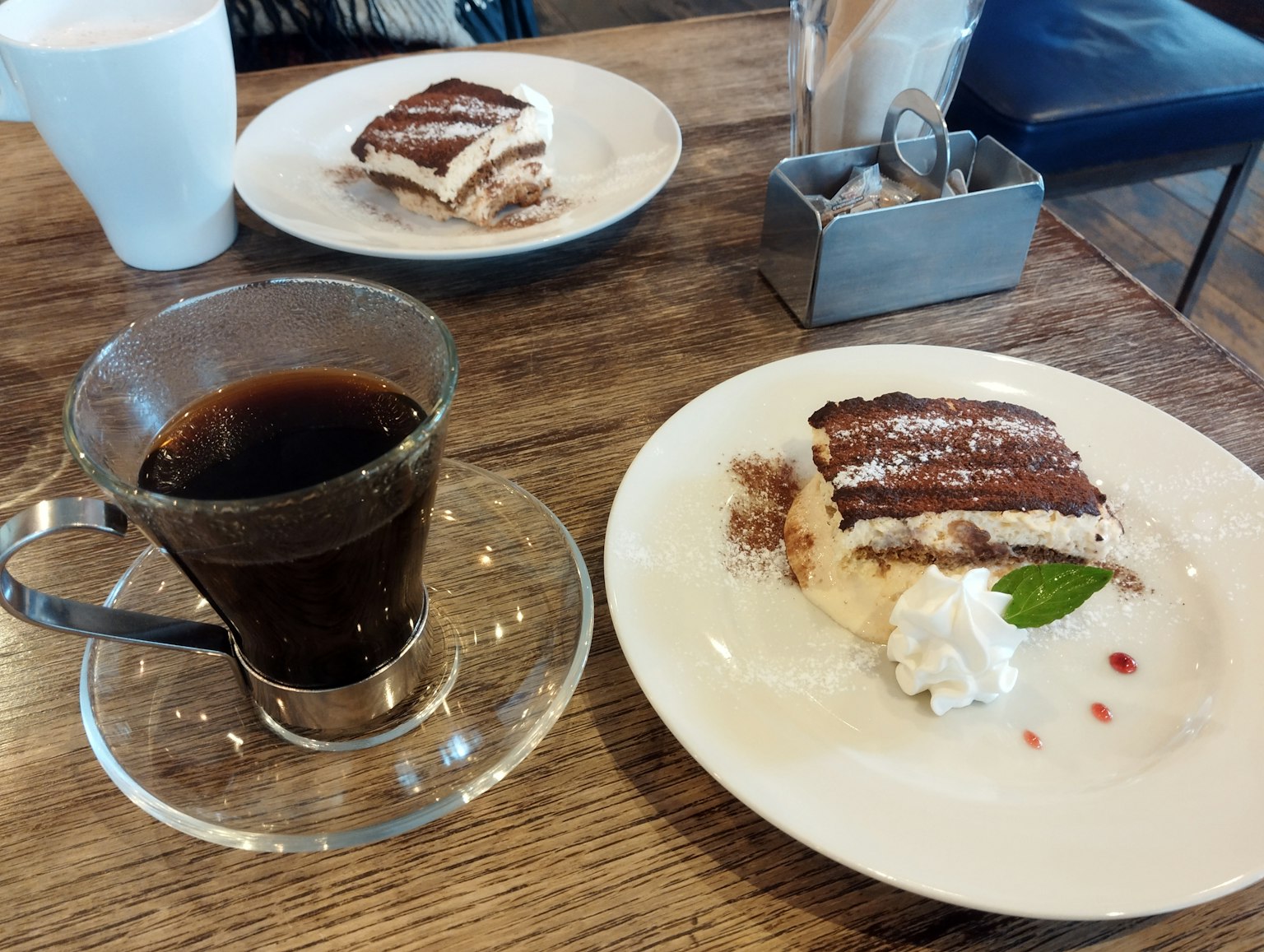 Eine Tasse Kaffee neben einem Stück Tiramisu auf einem Holztisch