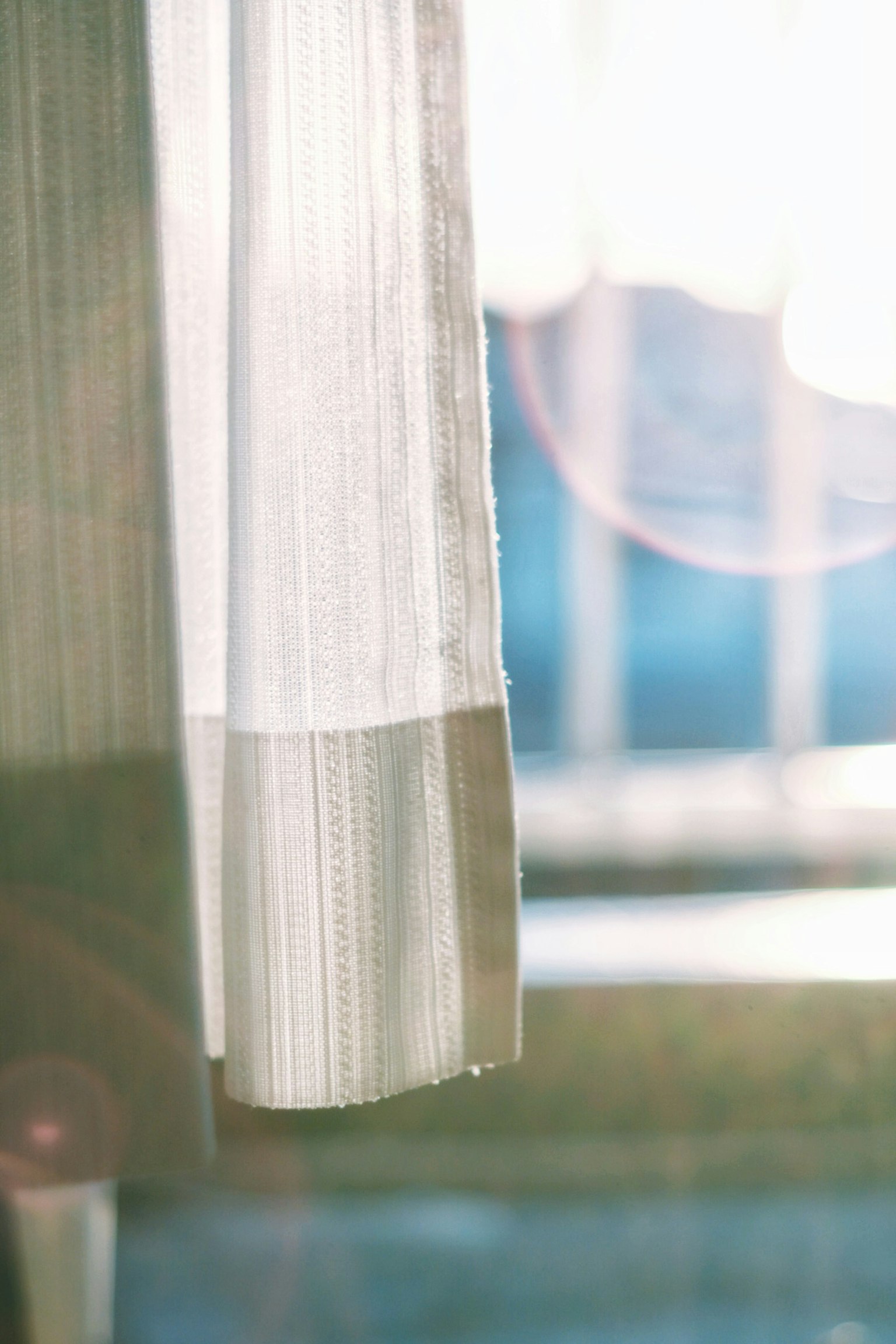 窓辺にかかる白いカーテンの一部と柔らかな光