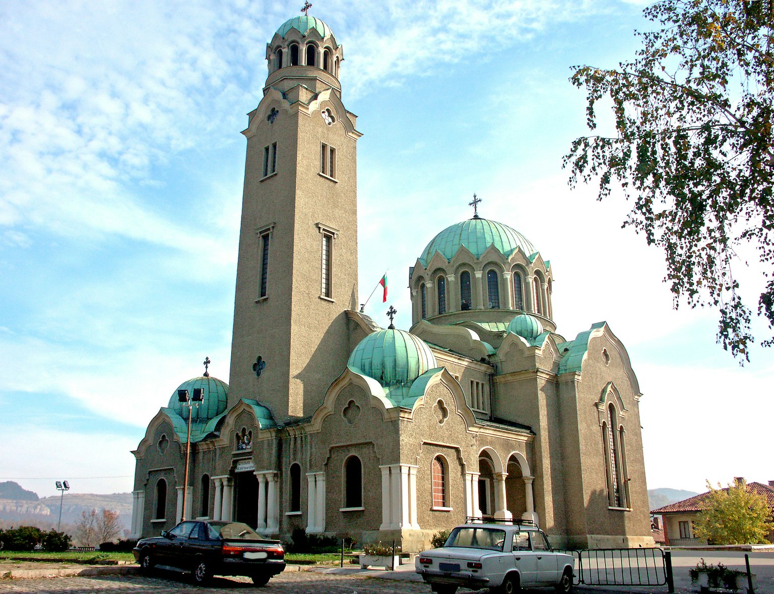 Exterior de una iglesia con cúpulas verdes y una torre alta