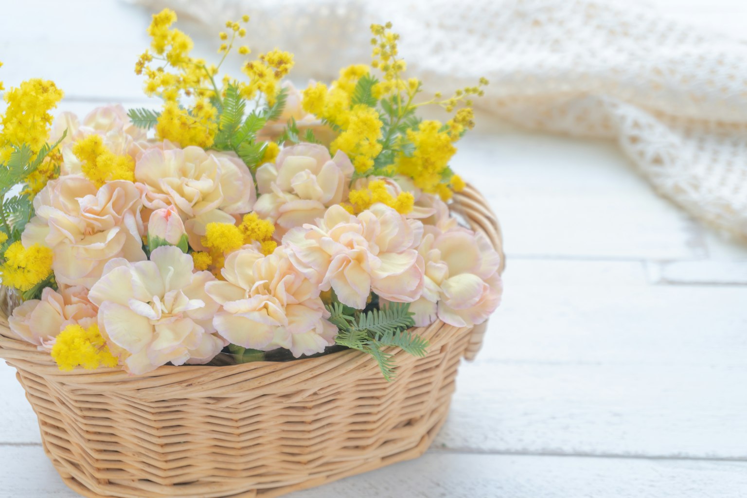 Un panier en osier rempli de fleurs roses et jaunes douces avec un tissu tricoté blanc