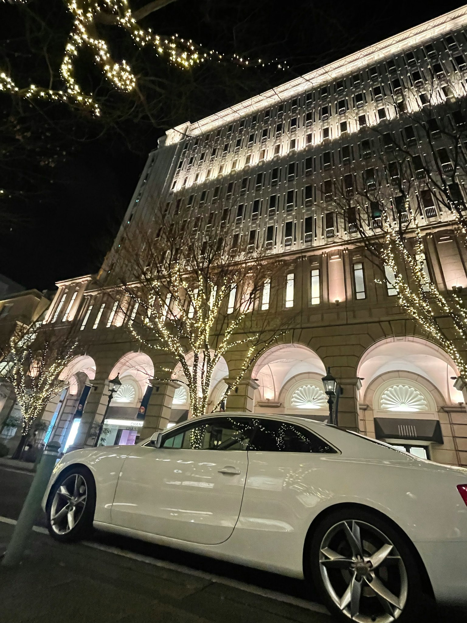 一輛優雅的白色汽車停在夜間美麗照明的建築旁