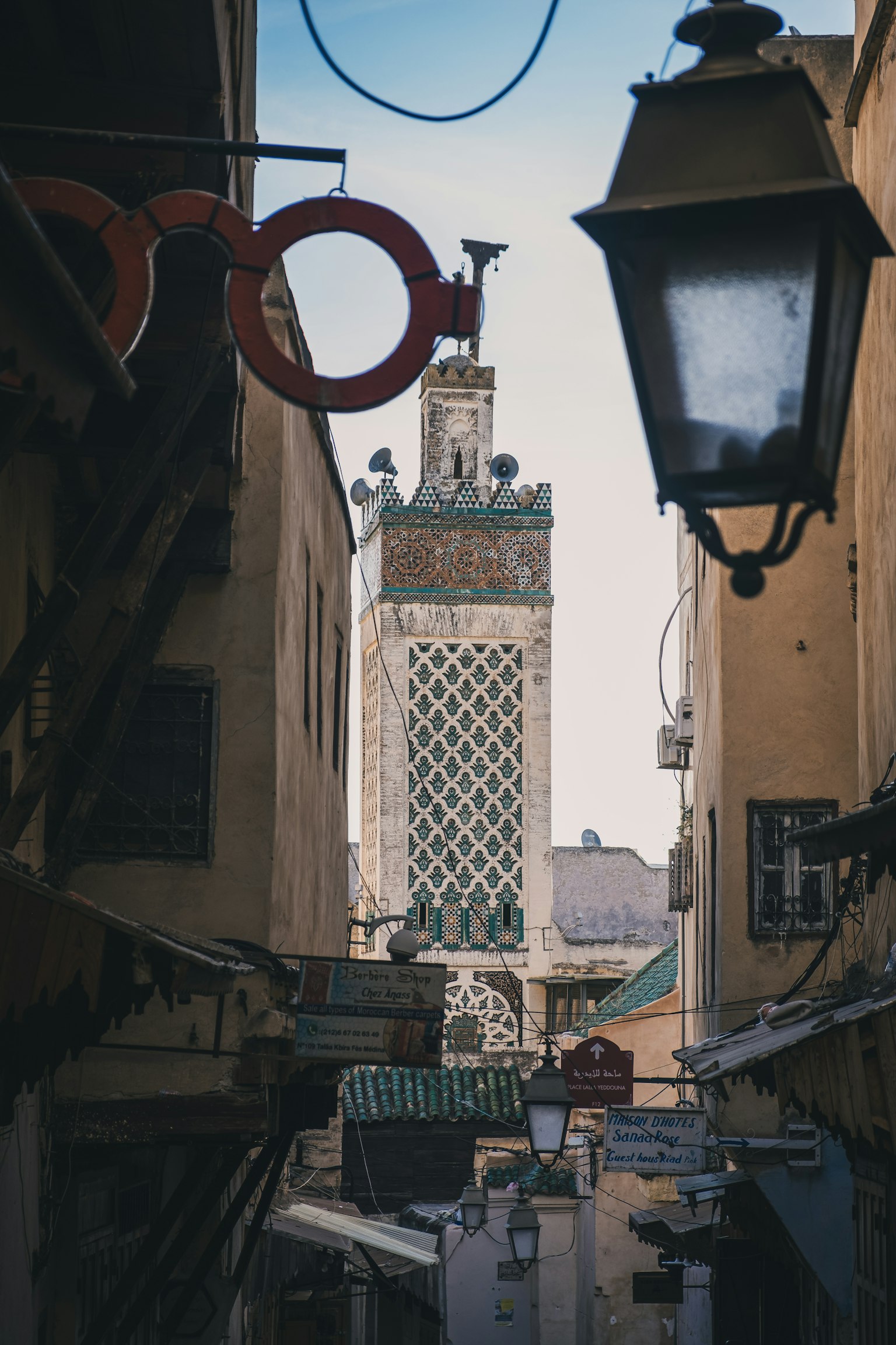 Ngõ hẹp với đèn và biển hiệu màu đỏ, tháp minaret của nhà thờ Hồi giáo ở phía xa