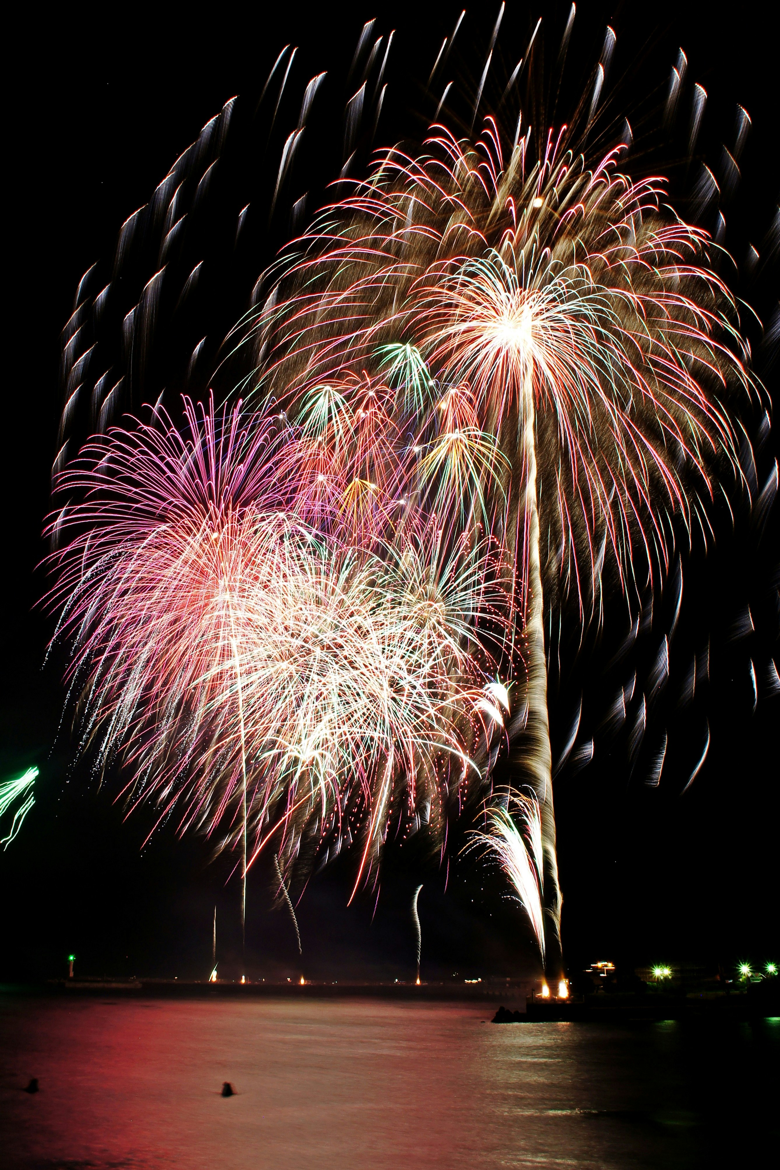 夜空に咲く色とりどりの花火と水面の反射