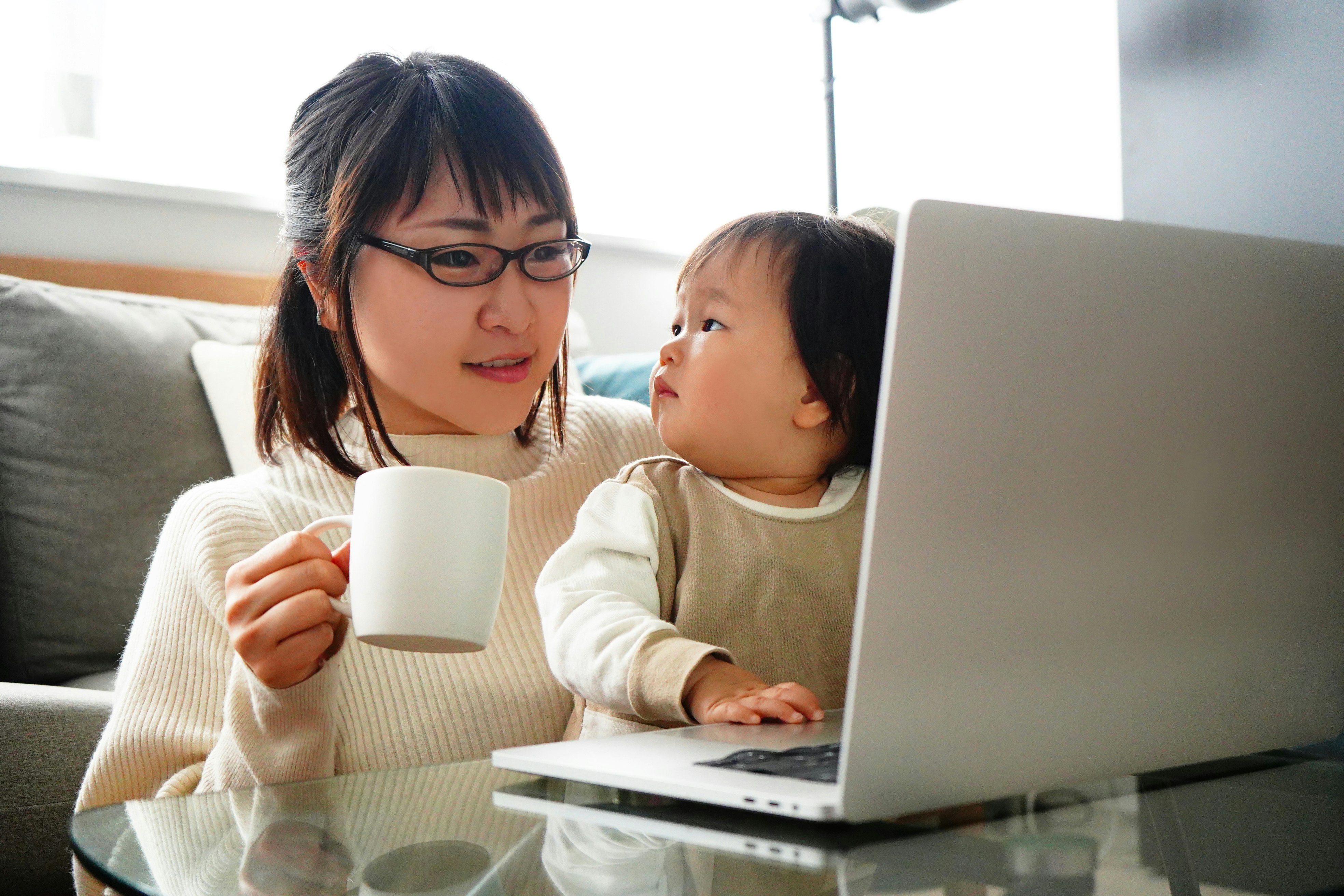 Genitore che tiene un bambino mentre lavora al computer portatile sul divano