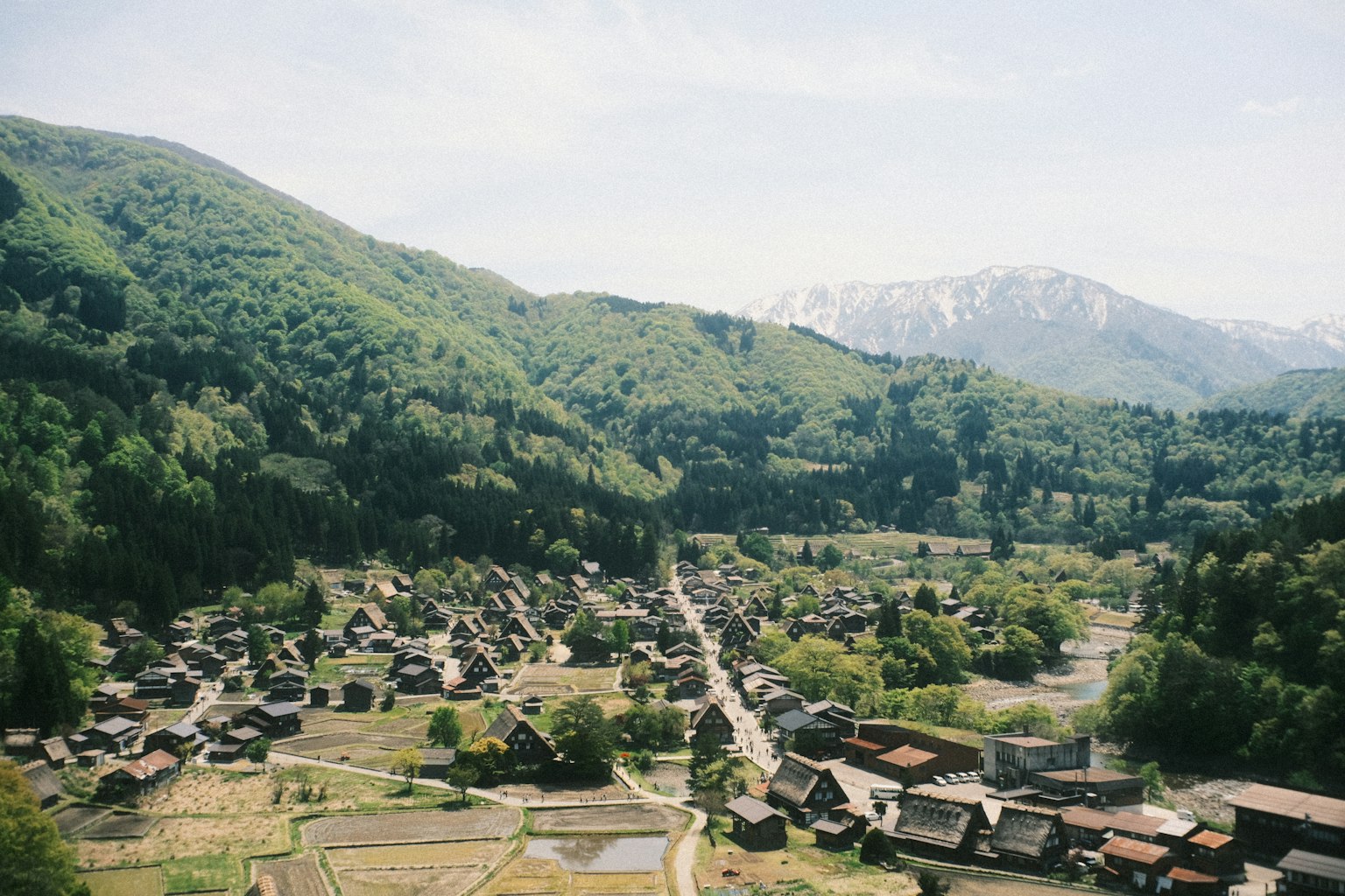 Vista panoramica di un villaggio circondato da montagne Colline verdi e picchi innevati sullo sfondo