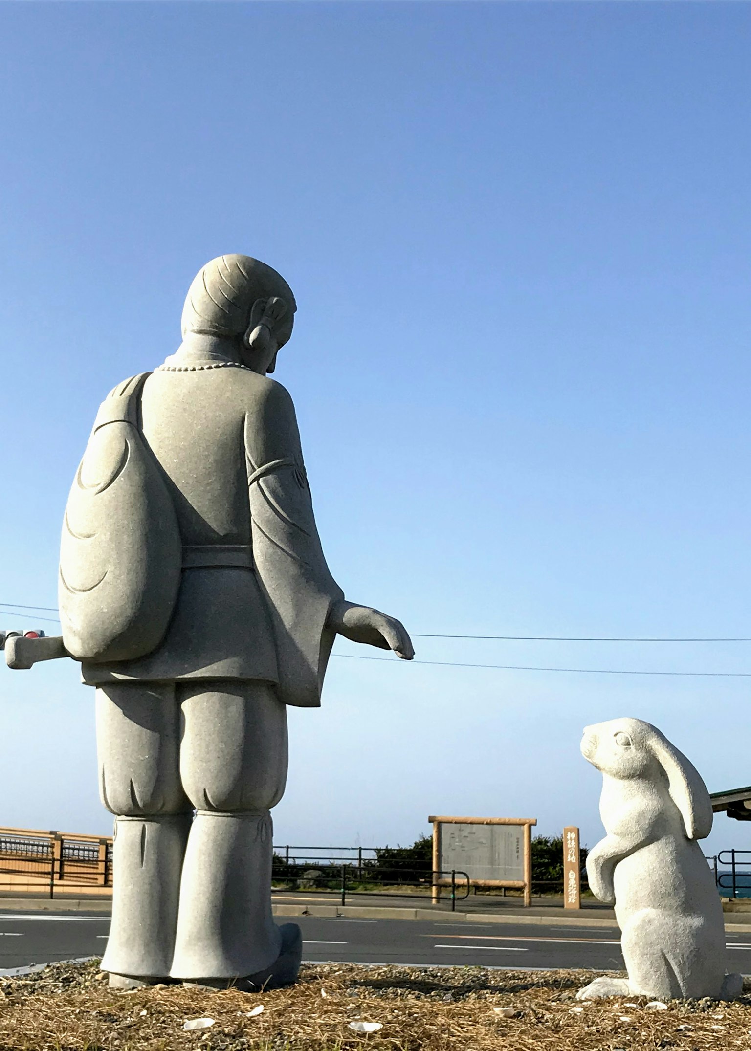 A statue of a person standing next to a rabbit statue against a blue sky