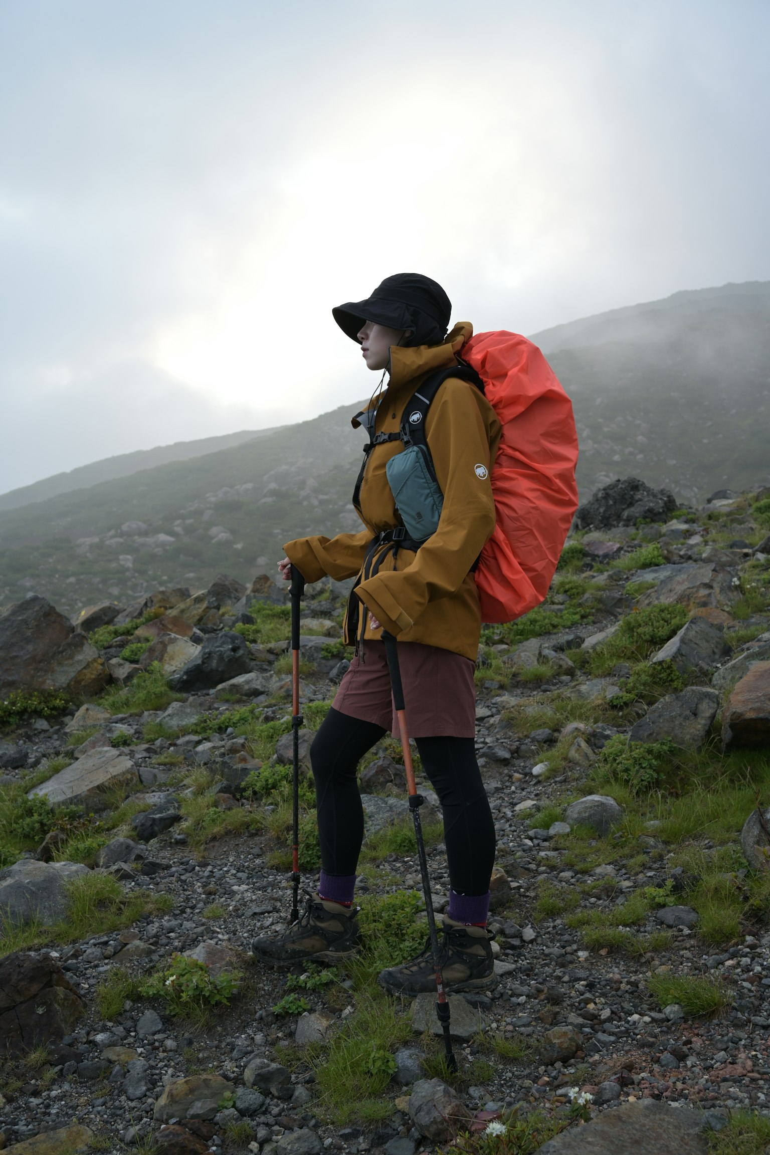 Silhouette di un escursionista nella nebbia con uno zaino arancione e bastoni da trekking