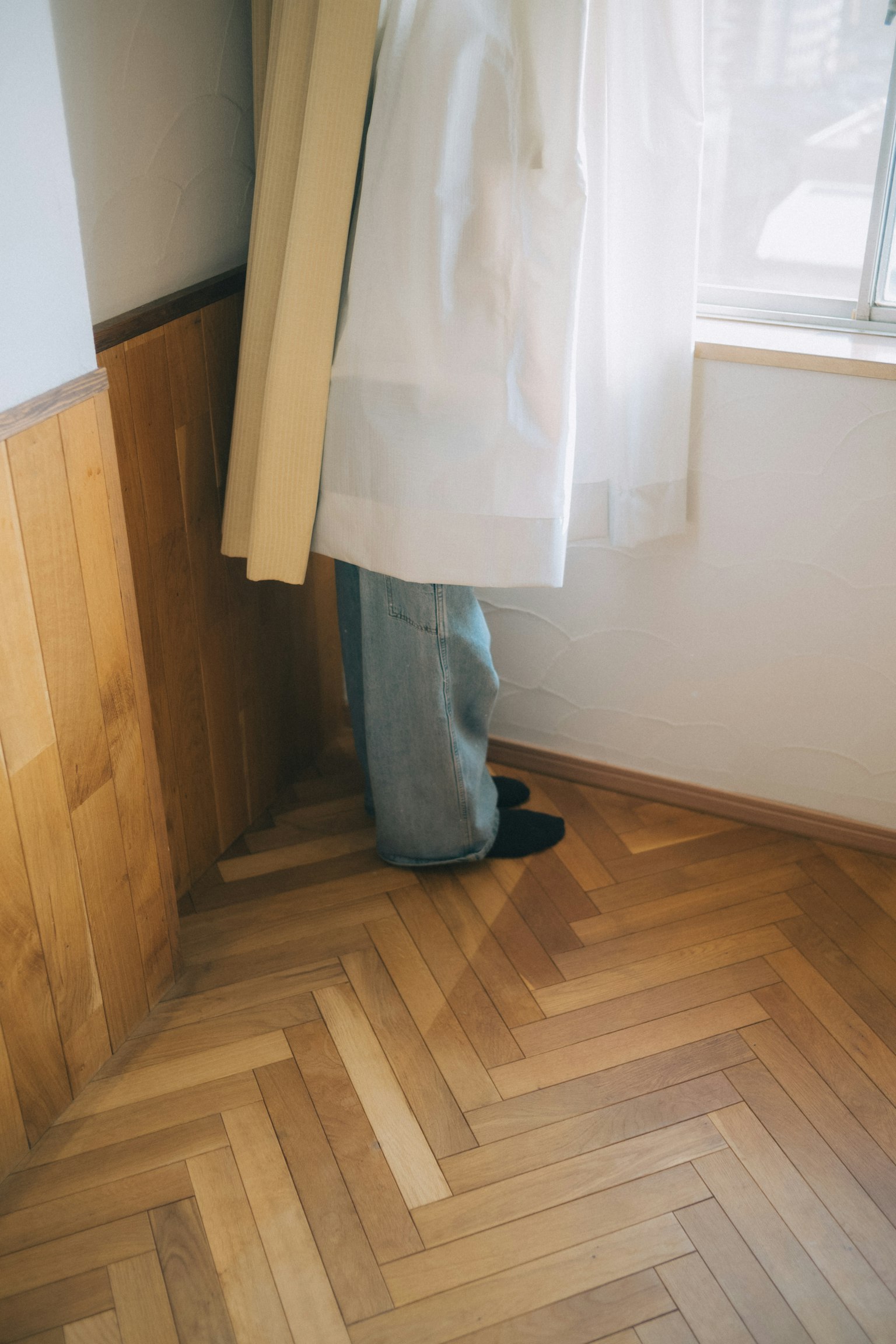 Piedi di una persona nascosti dietro una tenda con pavimento in legno
