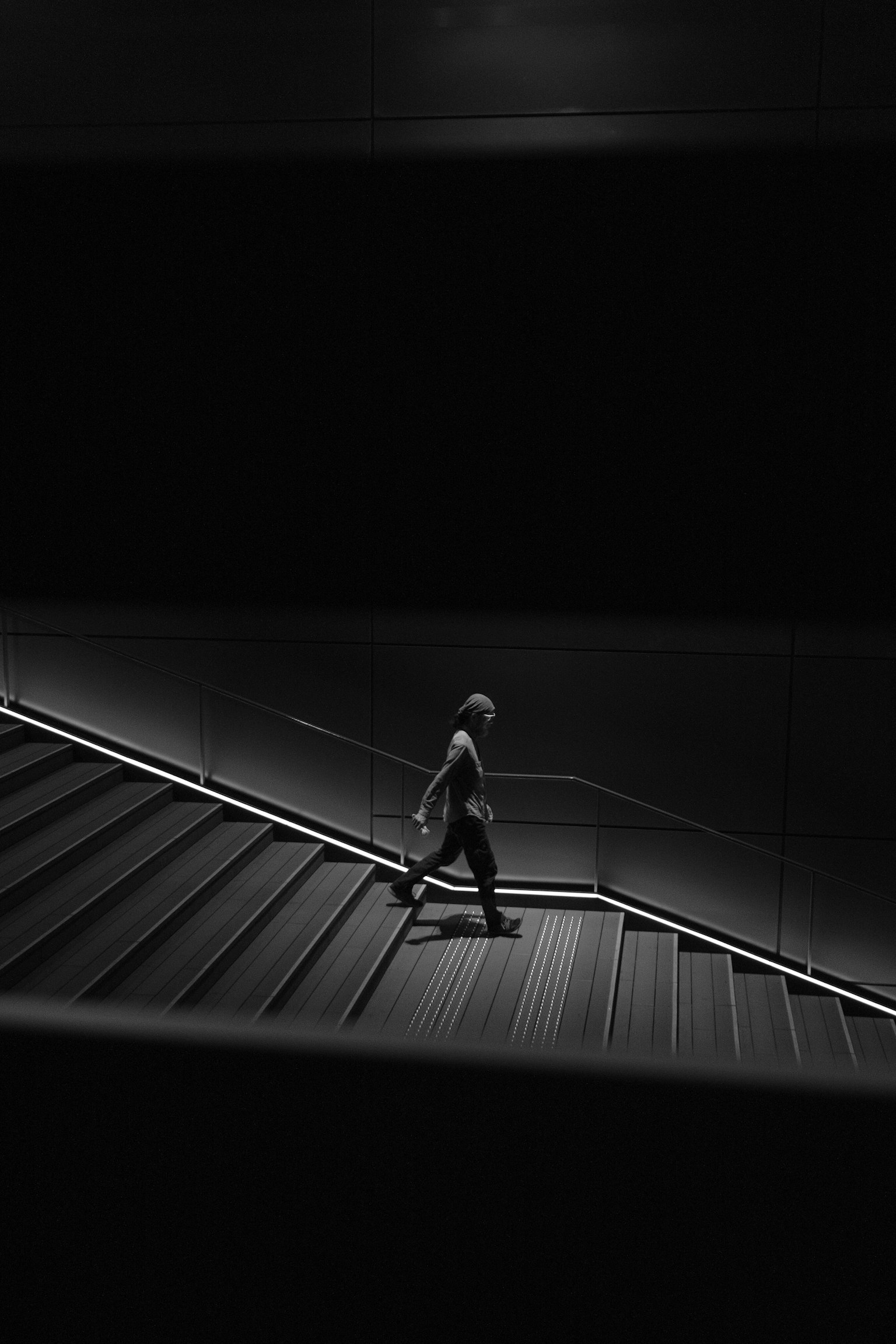 Schwarzweißfoto einer Person, die eine Treppe hinuntergeht, beleuchtet von sanftem Licht