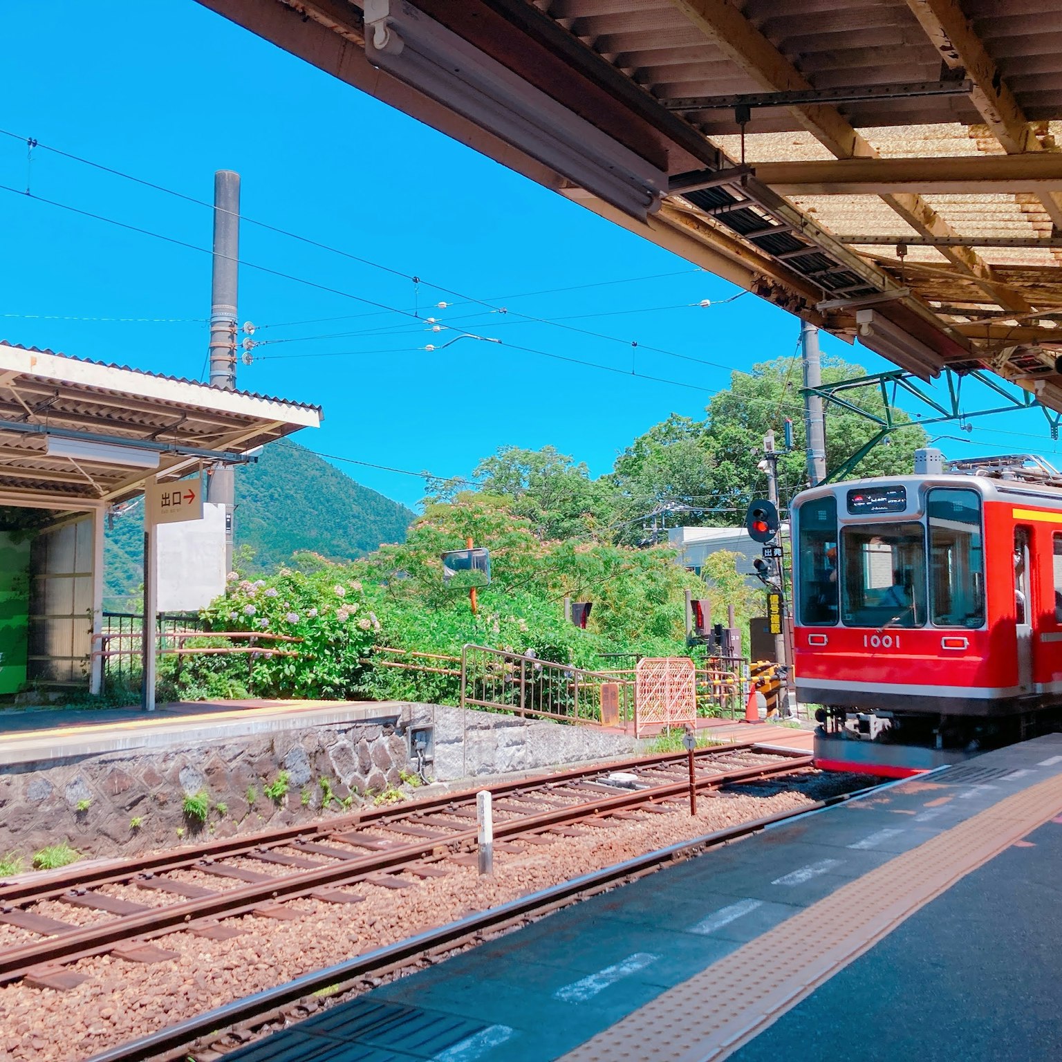Kereta merah berhenti di bawah langit biru dengan pemandangan hijau