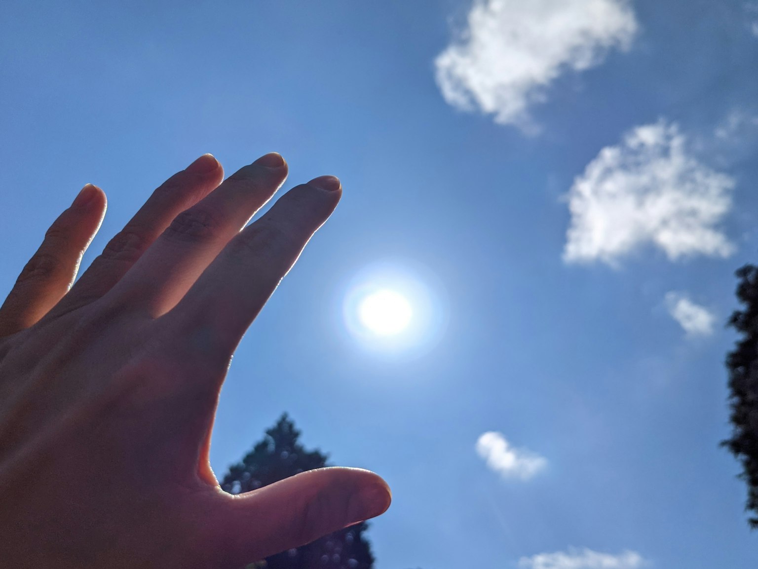 มือที่ยื่นไปยังดวงอาทิตย์ที่สว่างในท้องฟ้าสีฟ้า