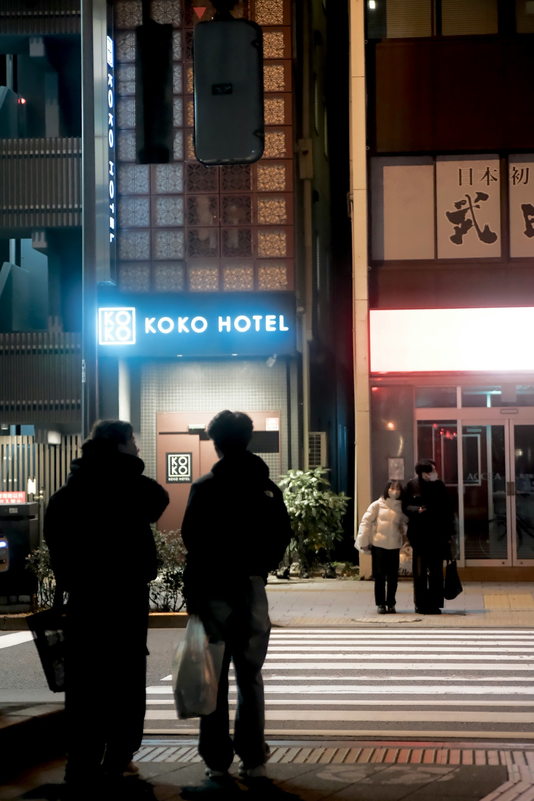夜の交差点でKOKO HOTELの前に立つ二人の人物