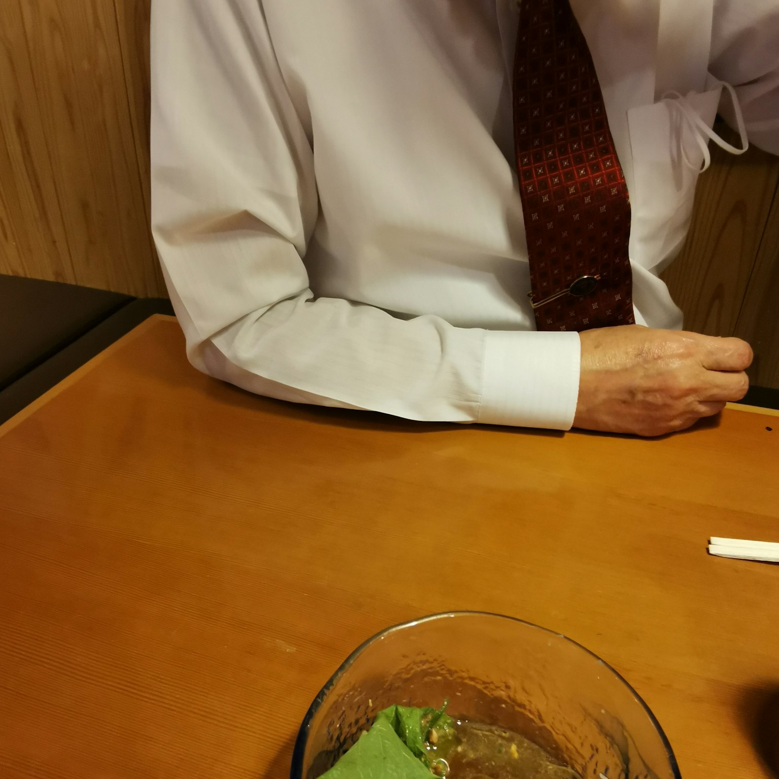 一位穿著白襯衫和紅色領帶的男性的手臂出現在桌子上的菜餚旁邊