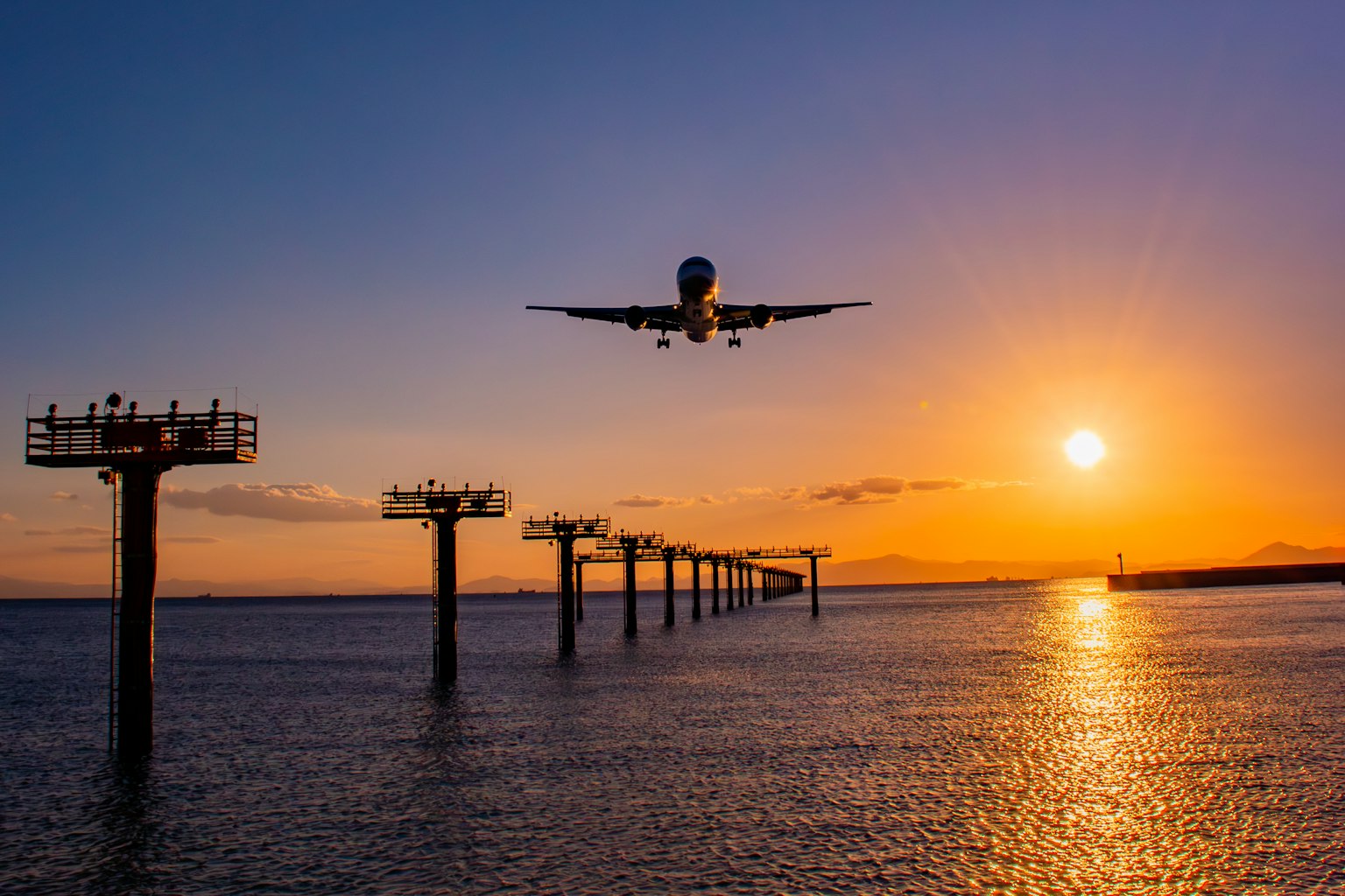 Aereo in avvicinamento al tramonto con riflessi sull'acqua e strutture del molo