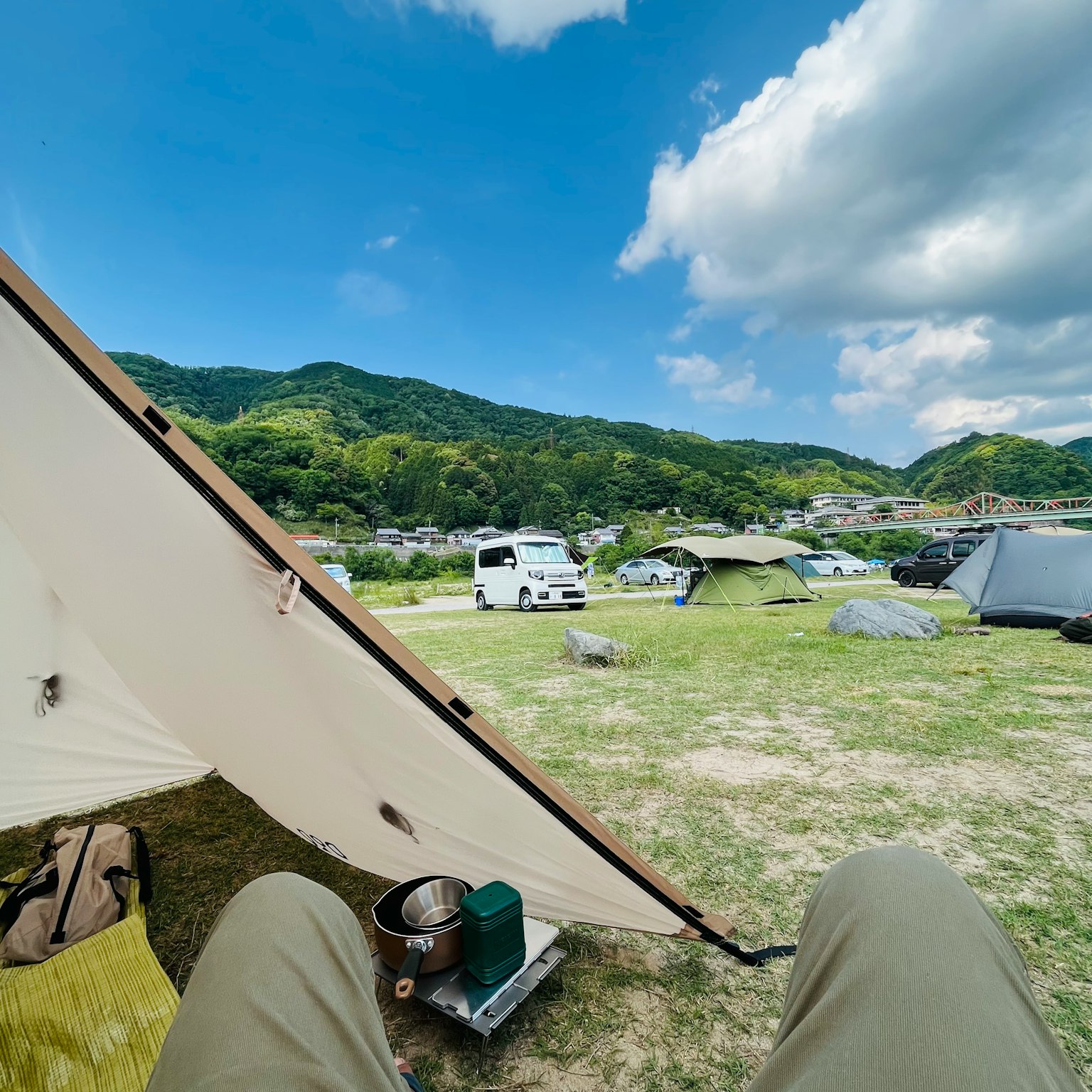 Scena di campeggio con cielo blu e montagne verdi tende e veicoli visibili