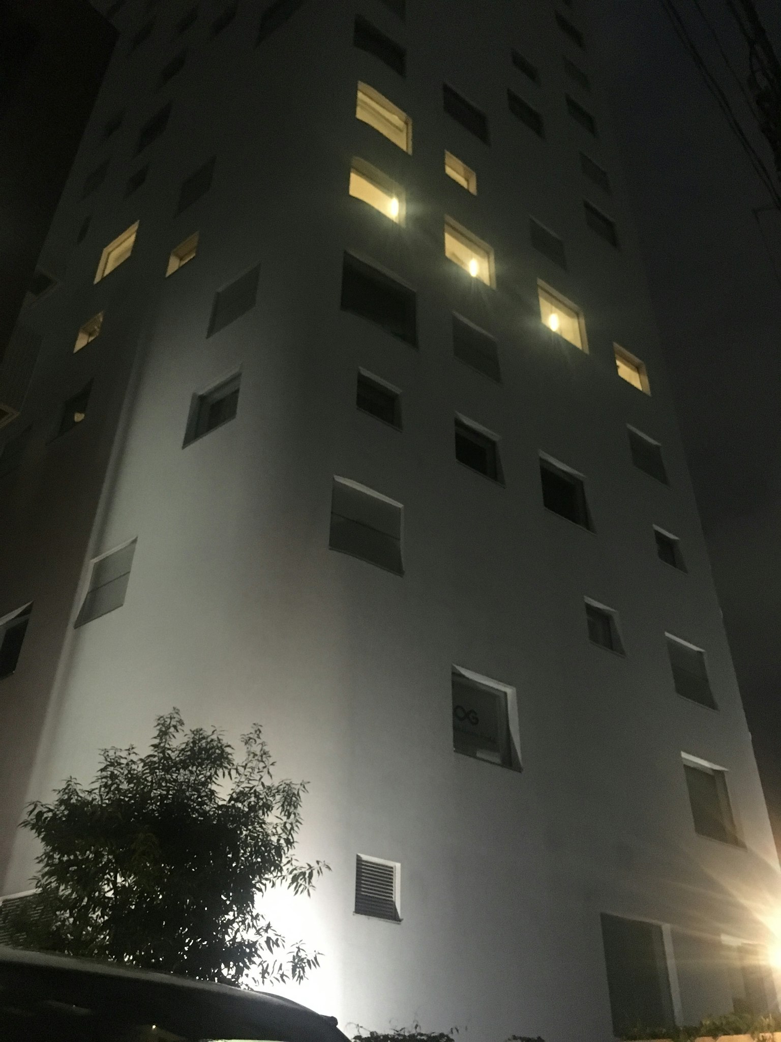Außenansicht eines Hochhauses bei Nacht mit beleuchteten Fenstern und umgebenden Bäumen