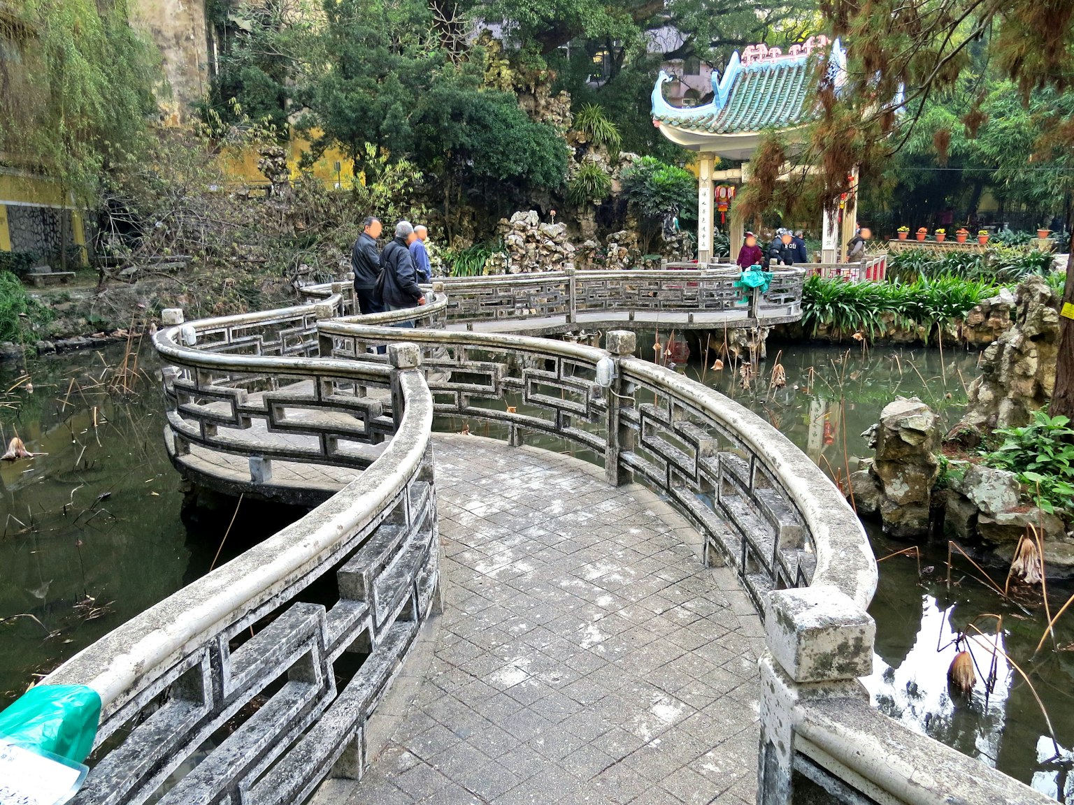Curved stone bridge in a serene garden with a pond and greenery