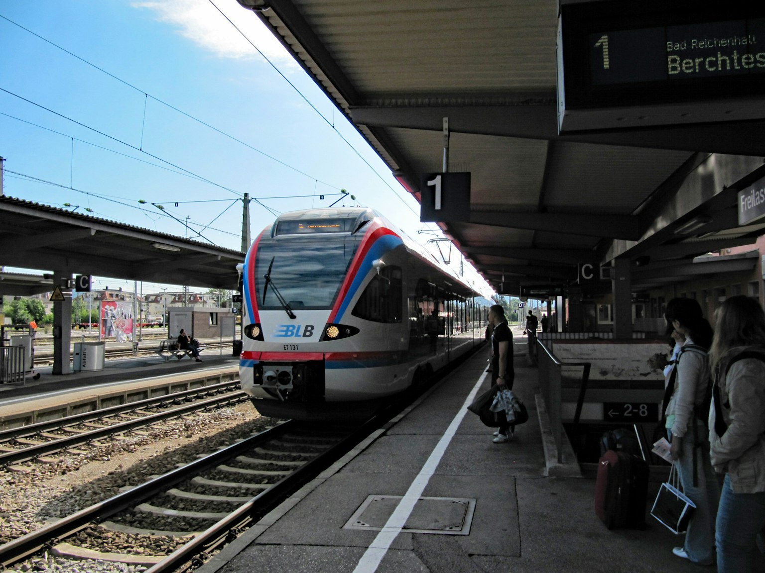 Zug, der an einem Bahnsteig mit wartenden Passagieren ankommt