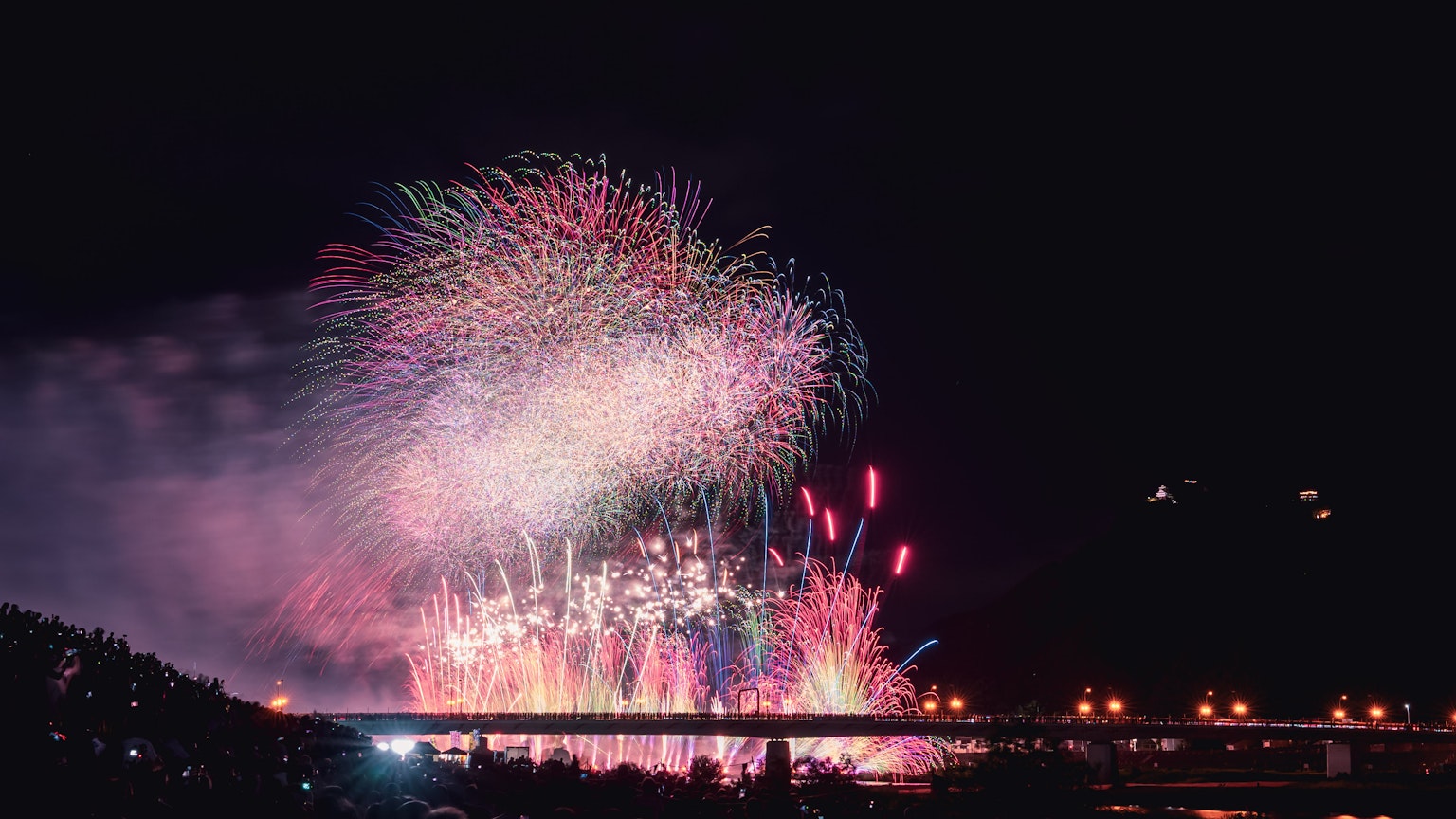 五彩繽紛的煙火表演照亮夜空，背景中有一座橋