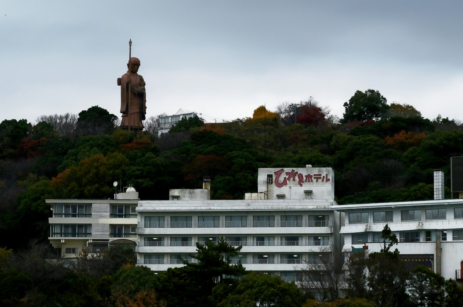 Riesenstatue auf einem Hügel umgeben von Grün und Gebäuden