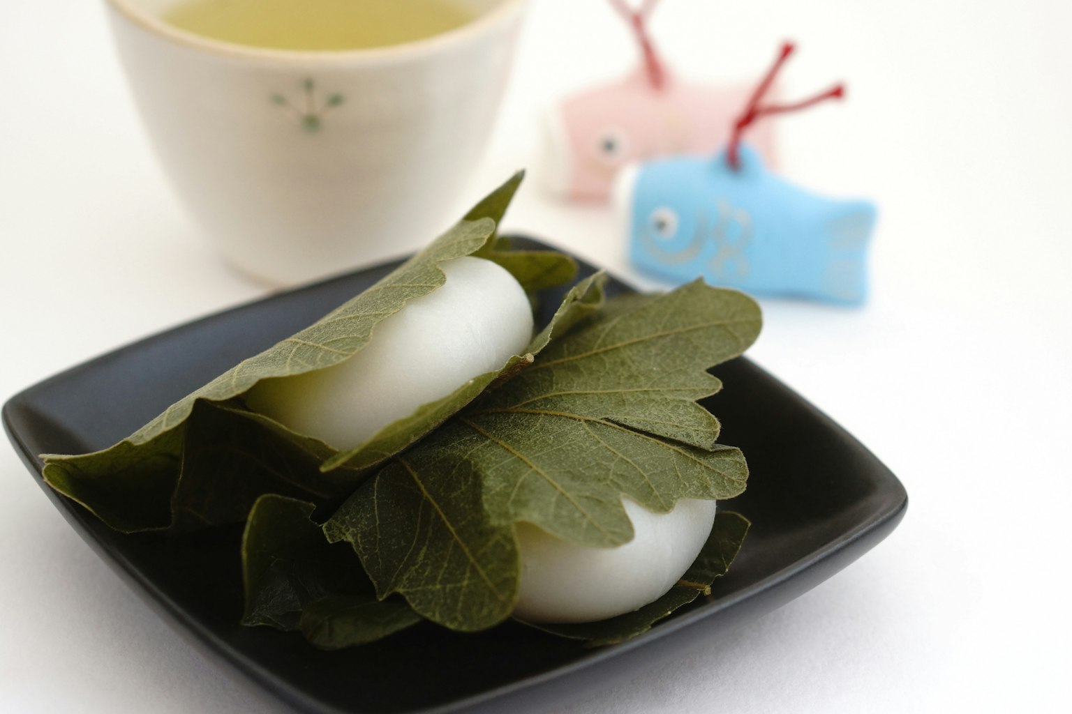 Piatto con dolci di riso bianchi avvolti in foglie accanto a una tazza di tè e oggetti decorativi colorati