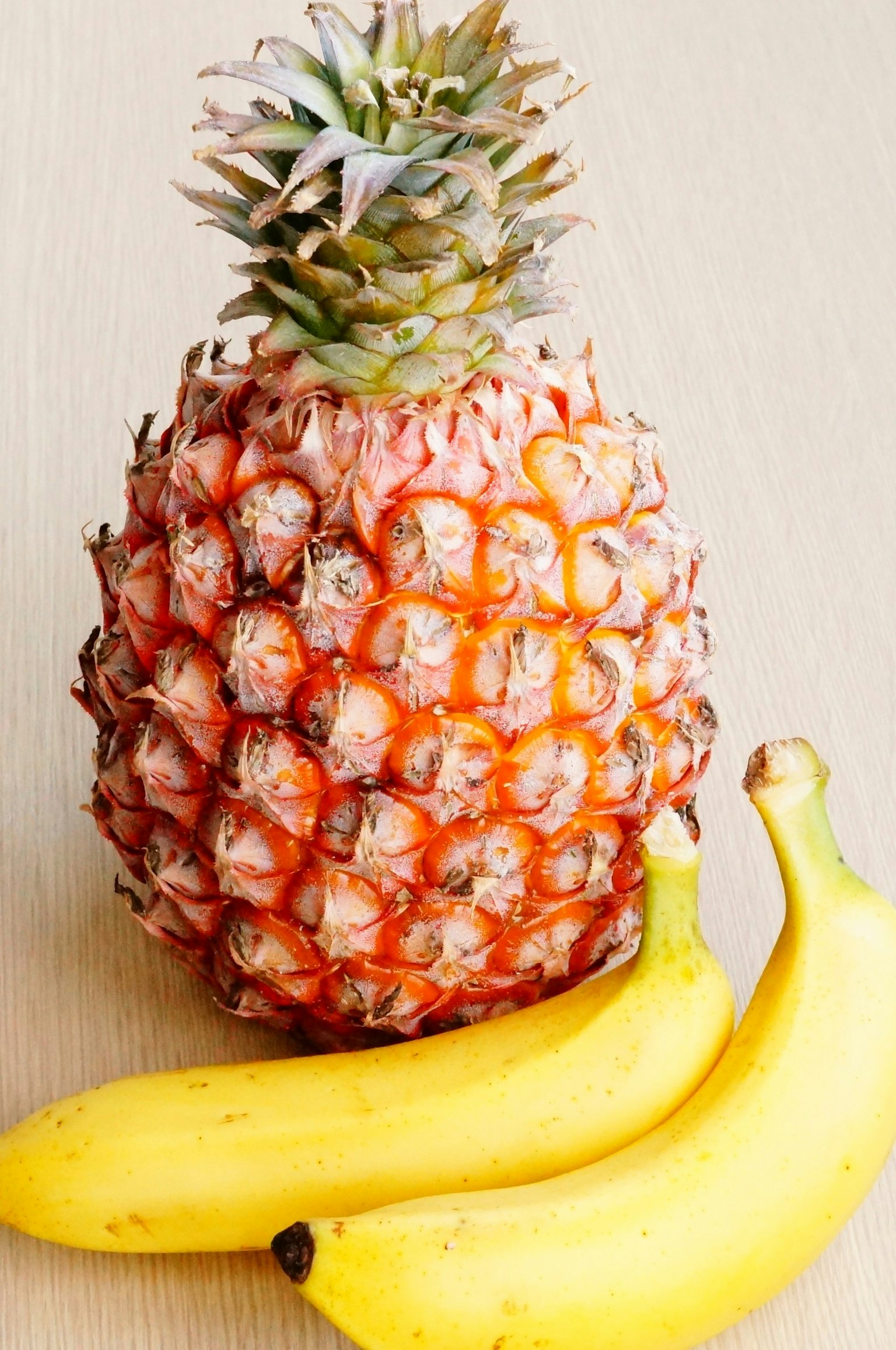 Una piña y dos plátanos sobre una superficie de madera