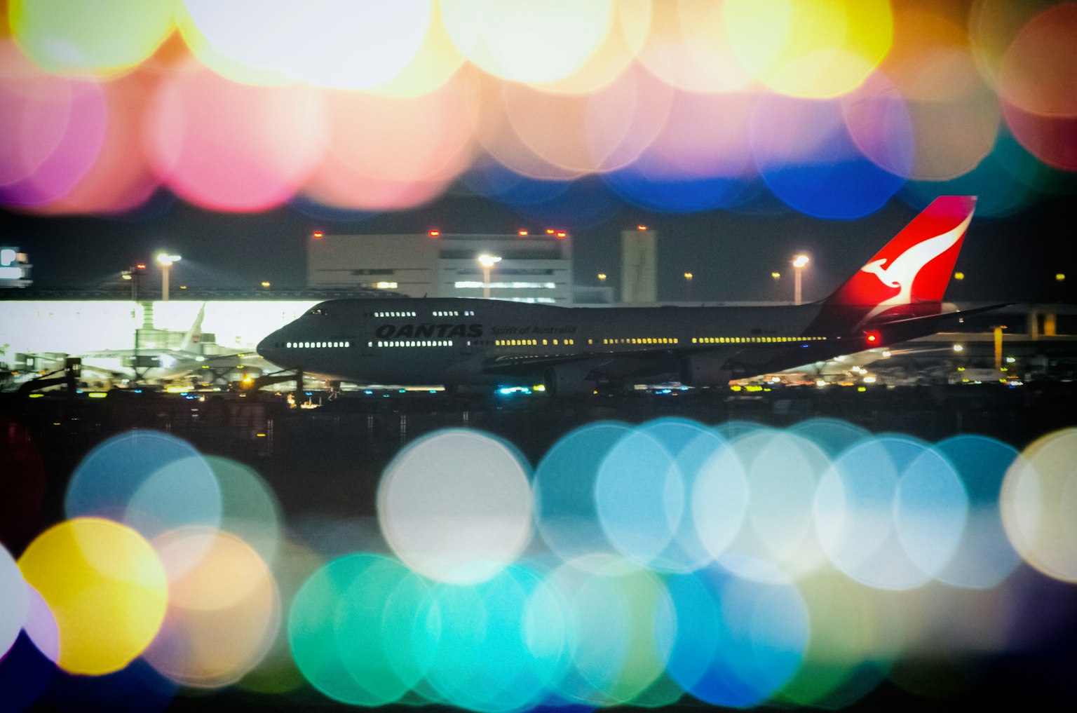 Qantas airplane silhouetted against a colorful bokeh background at night