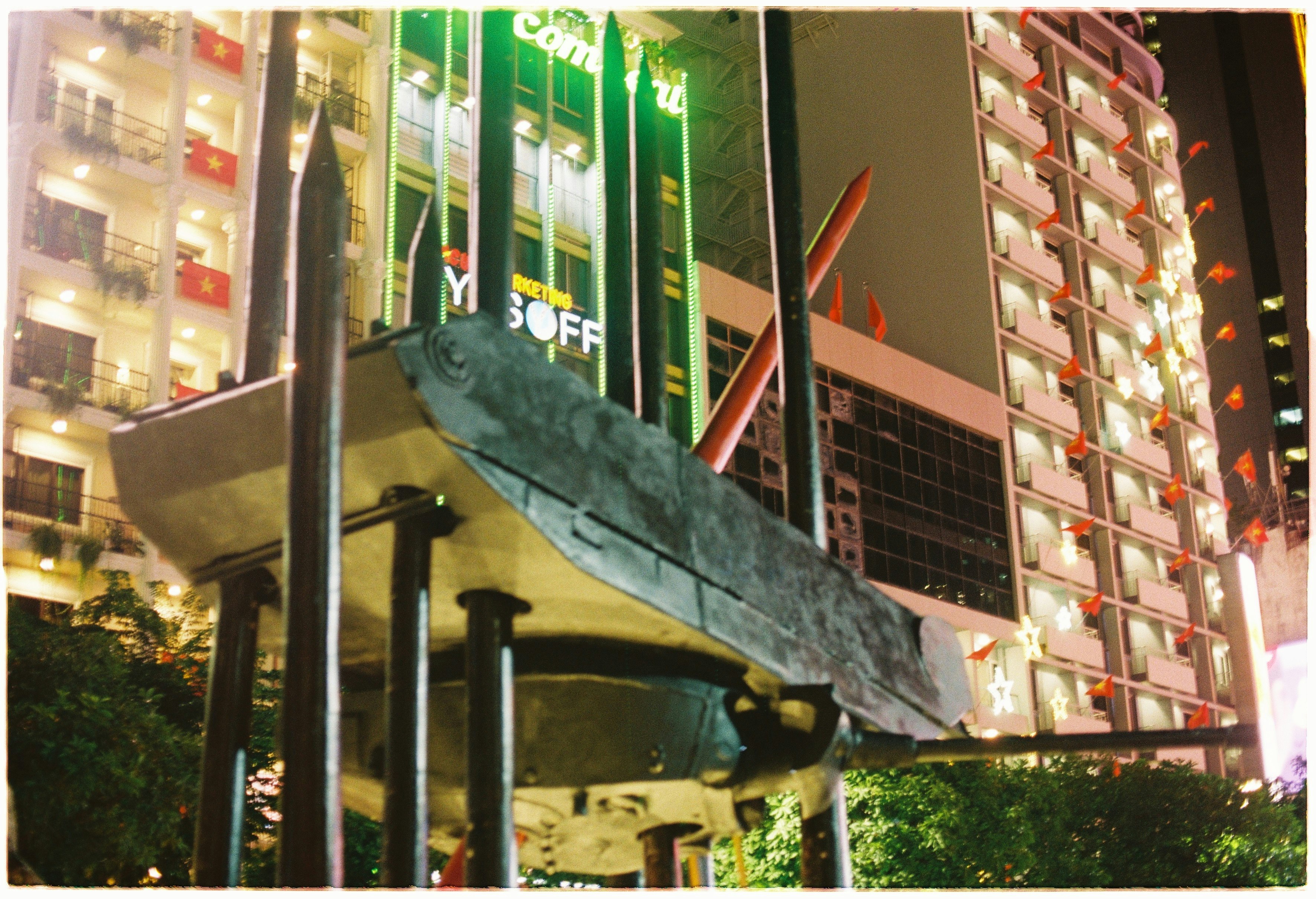 夜の街角に並ぶ看板とガラス張りの建物の前のベンチ