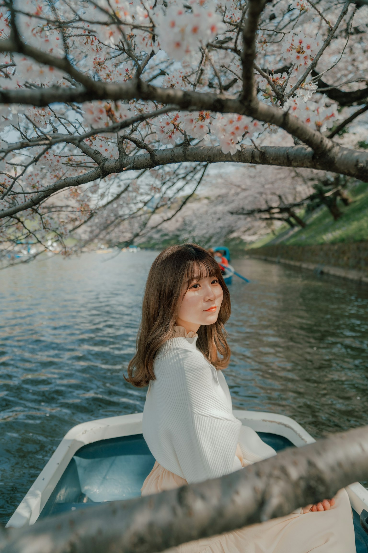 一位女性坐在小船上，樱花树下安静的河边