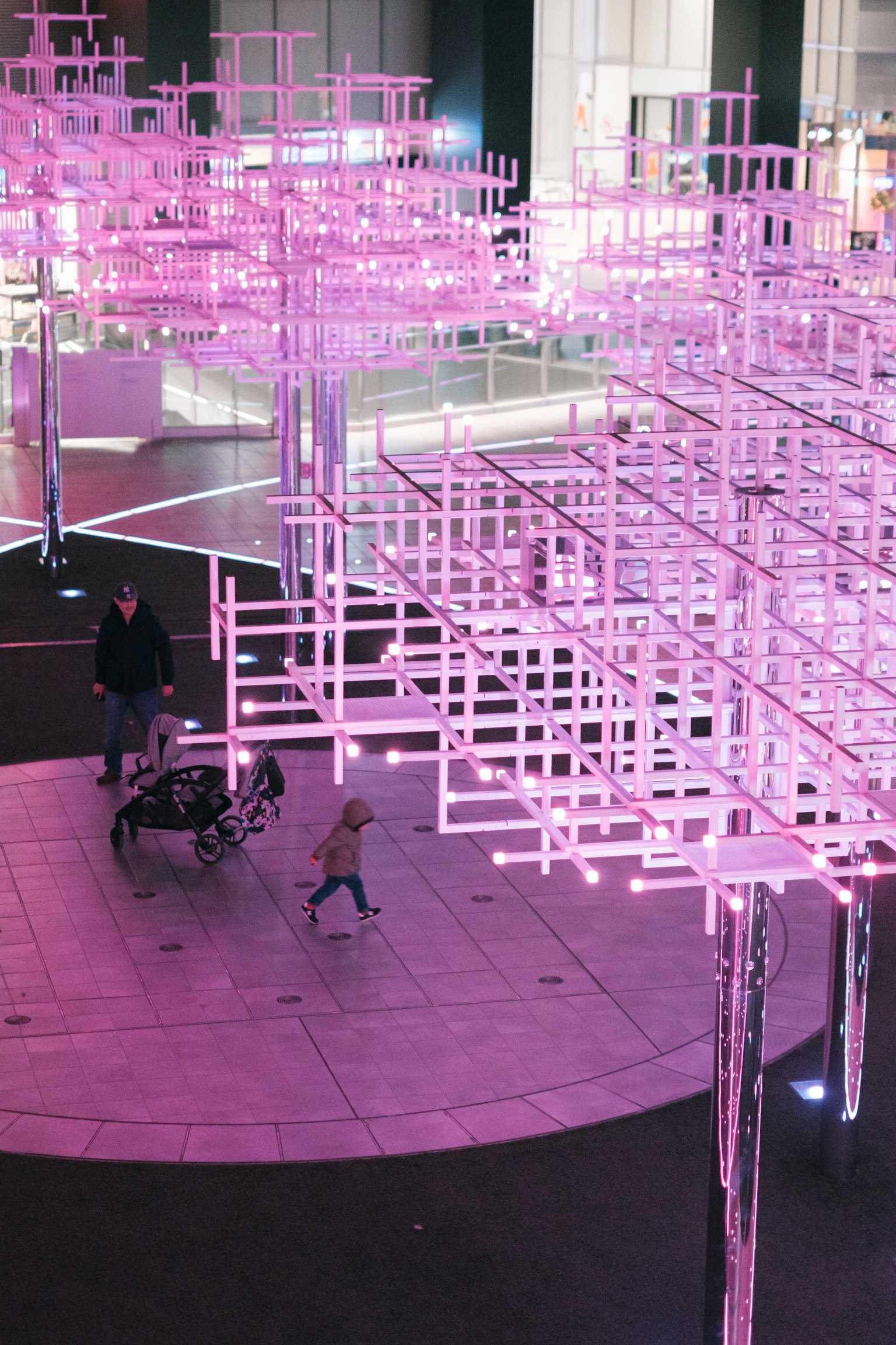 Orang-orang berjalan di bawah instalasi seni modern yang diterangi cahaya pink