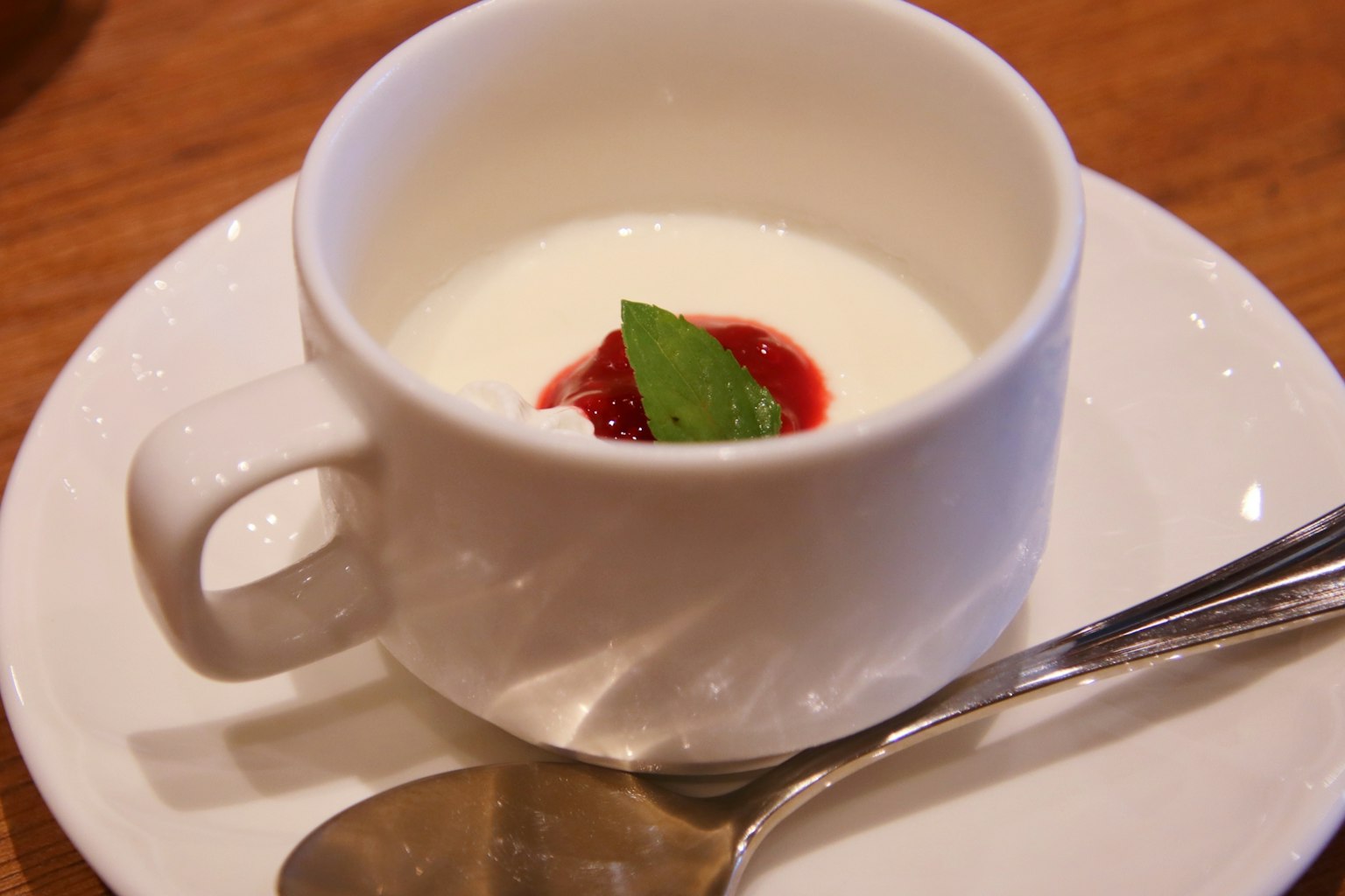 Dessert cremoso in una tazza bianca guarnito con salsa di fragole e una foglia di menta