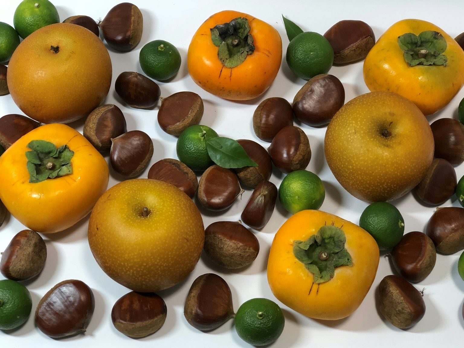 Una mezcla de caquis naranjas y limas verdes rodeados de castañas marrones