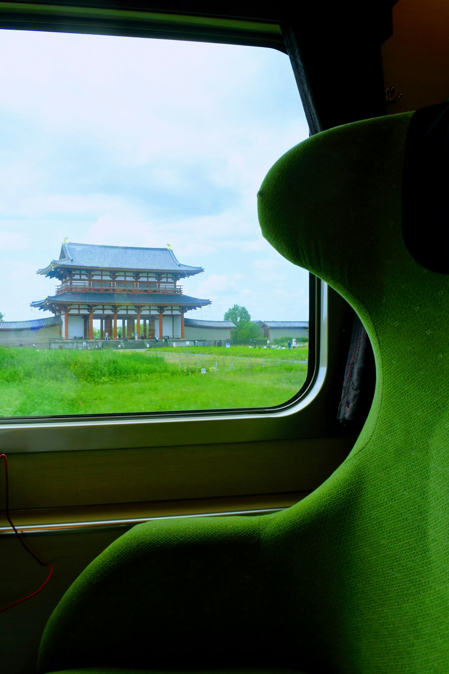 View from a train window featuring a green chair and an ancient building