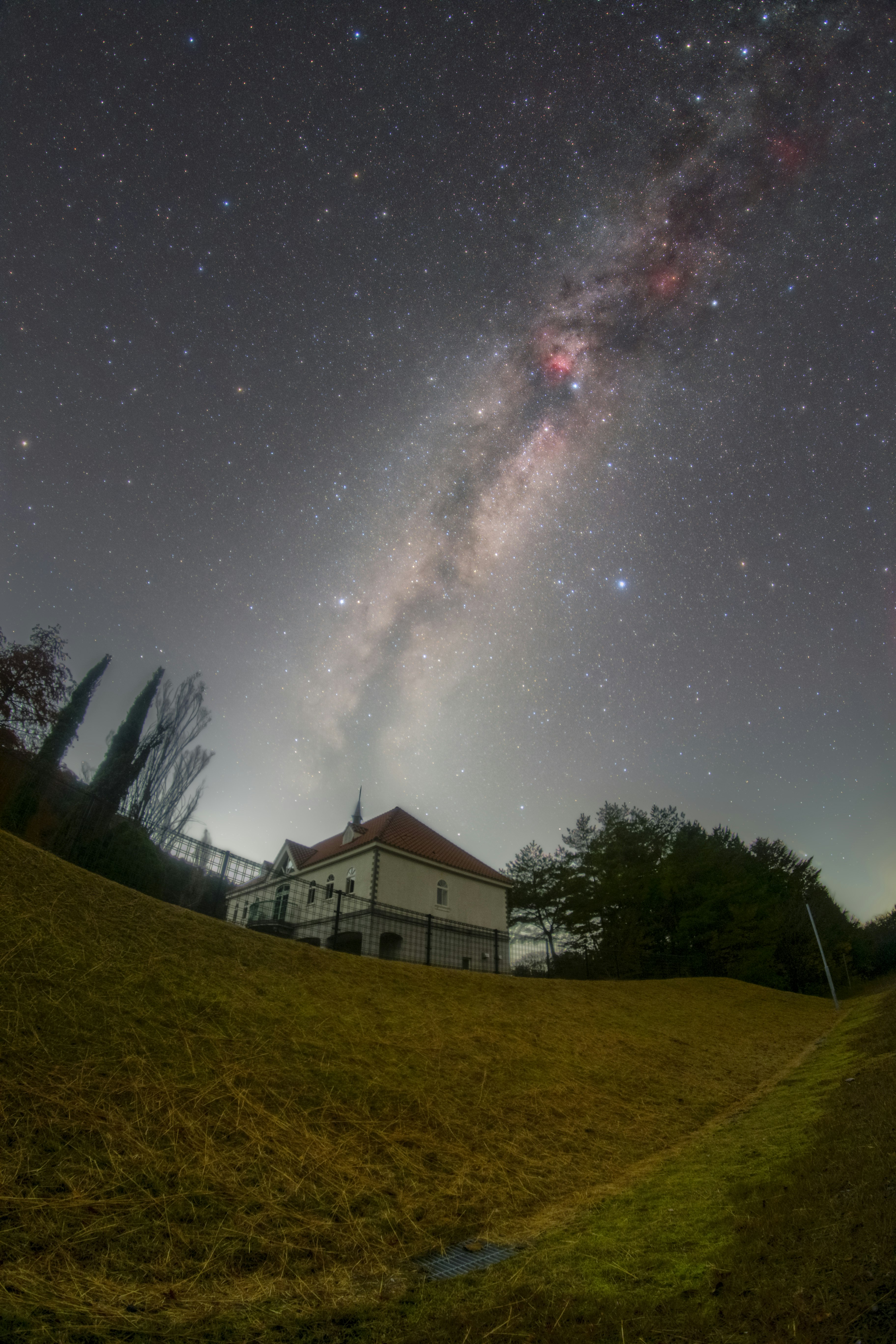 丘の上の建物と夜空に広がる天の川