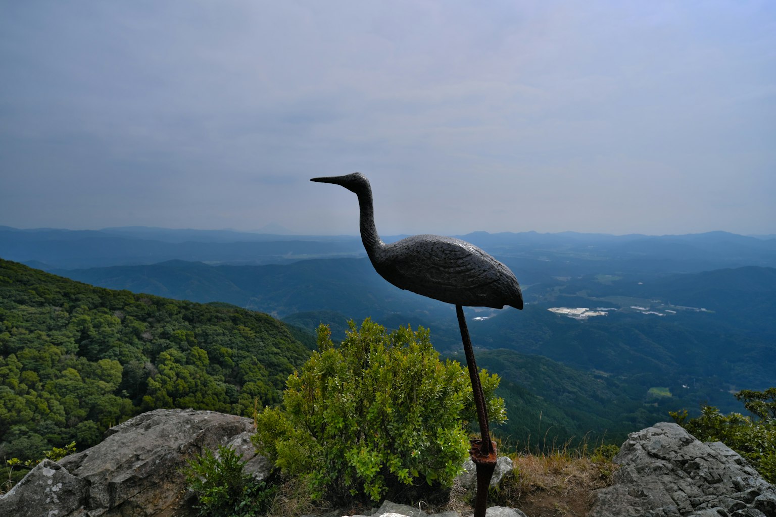 Metallskulptur eines Kranichs auf einem Berggipfel mit malerischer Aussicht