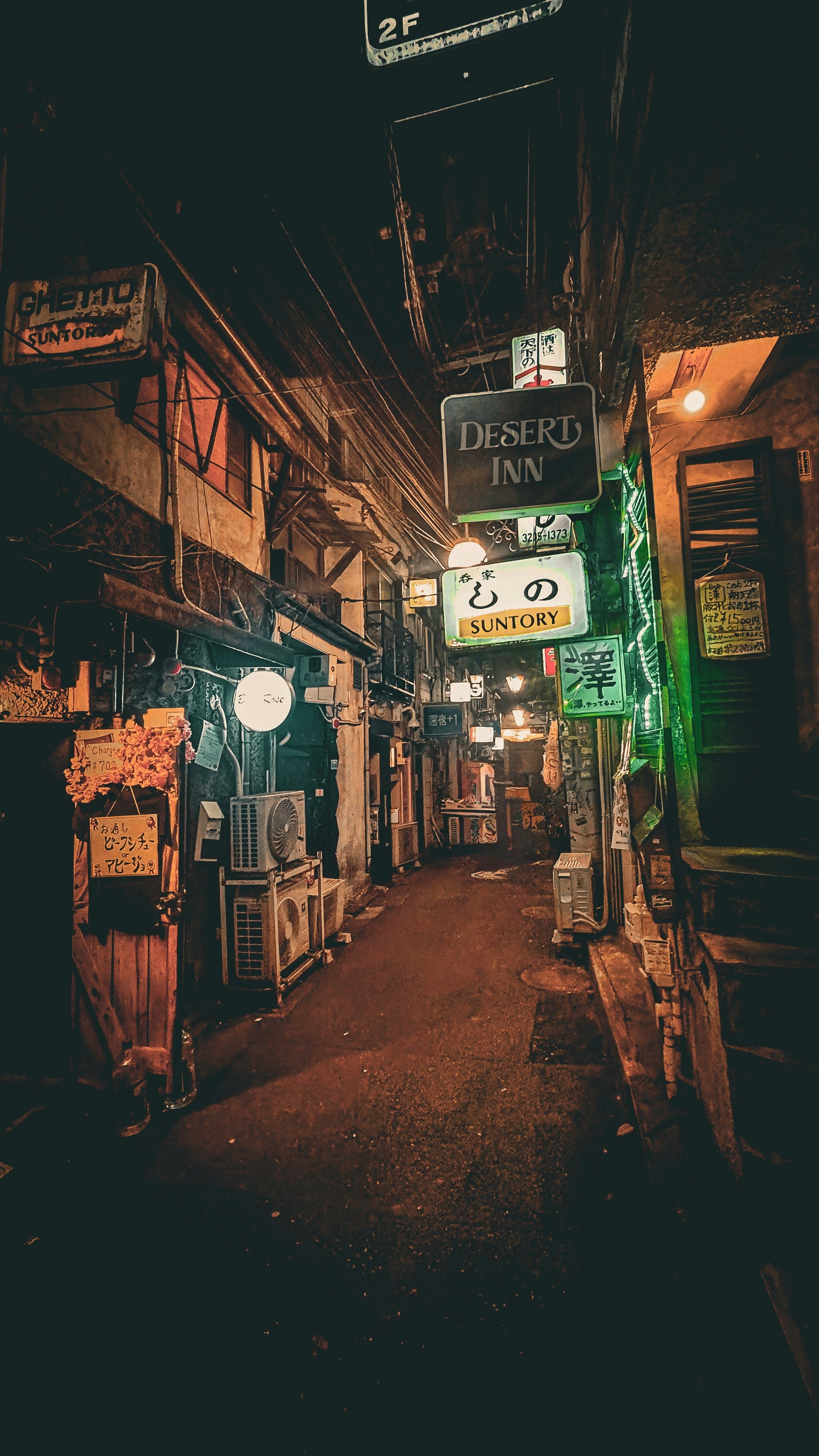 路地に並ぶ看板とネオンのある宿の外観