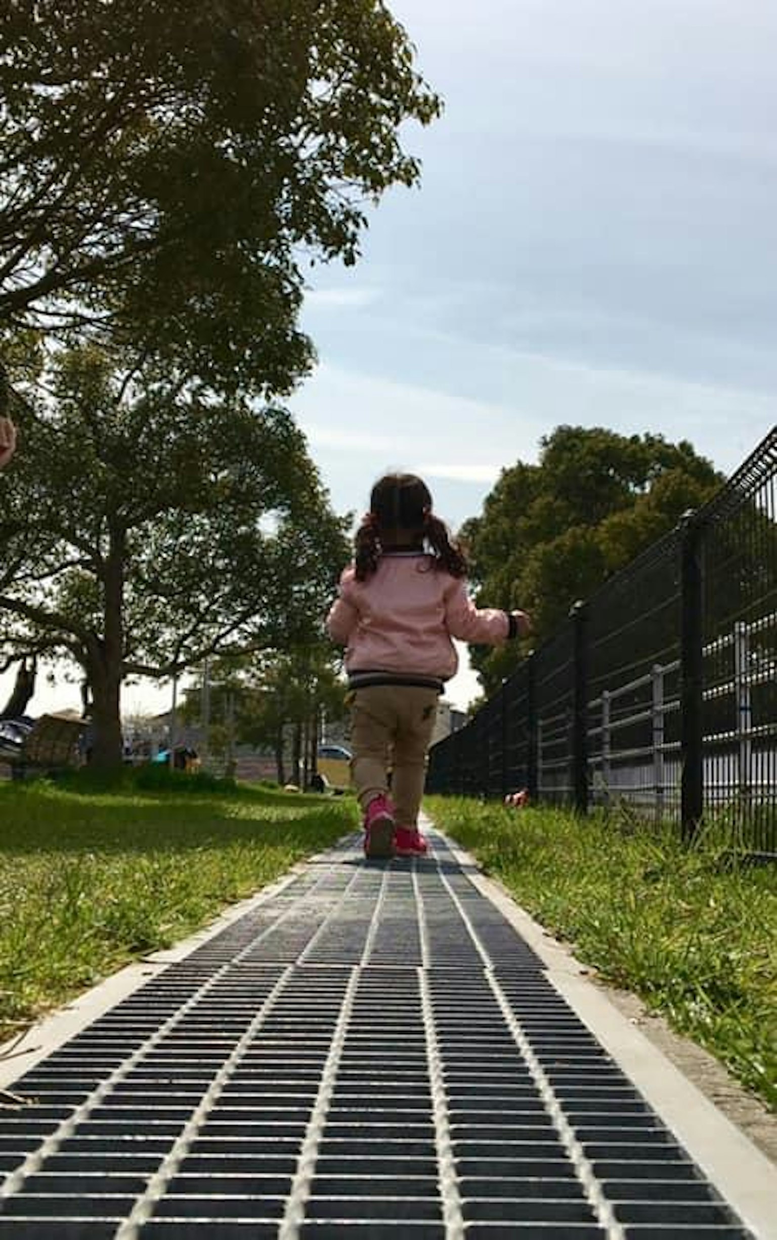 Una bambina piccola che cammina su un sentiero del parco vista da dietro