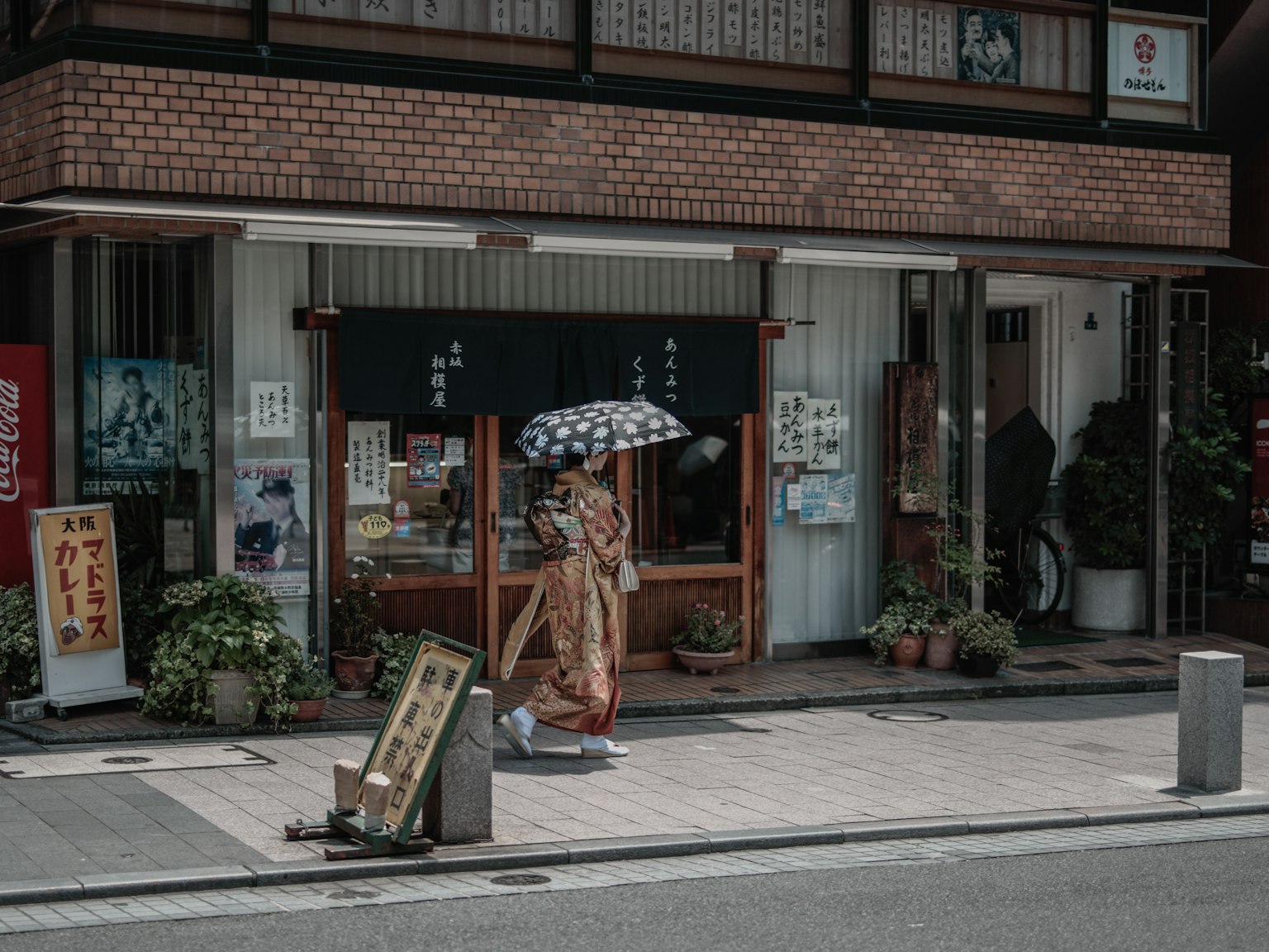 A woman in traditional kimono holding an umbrella in front of a store