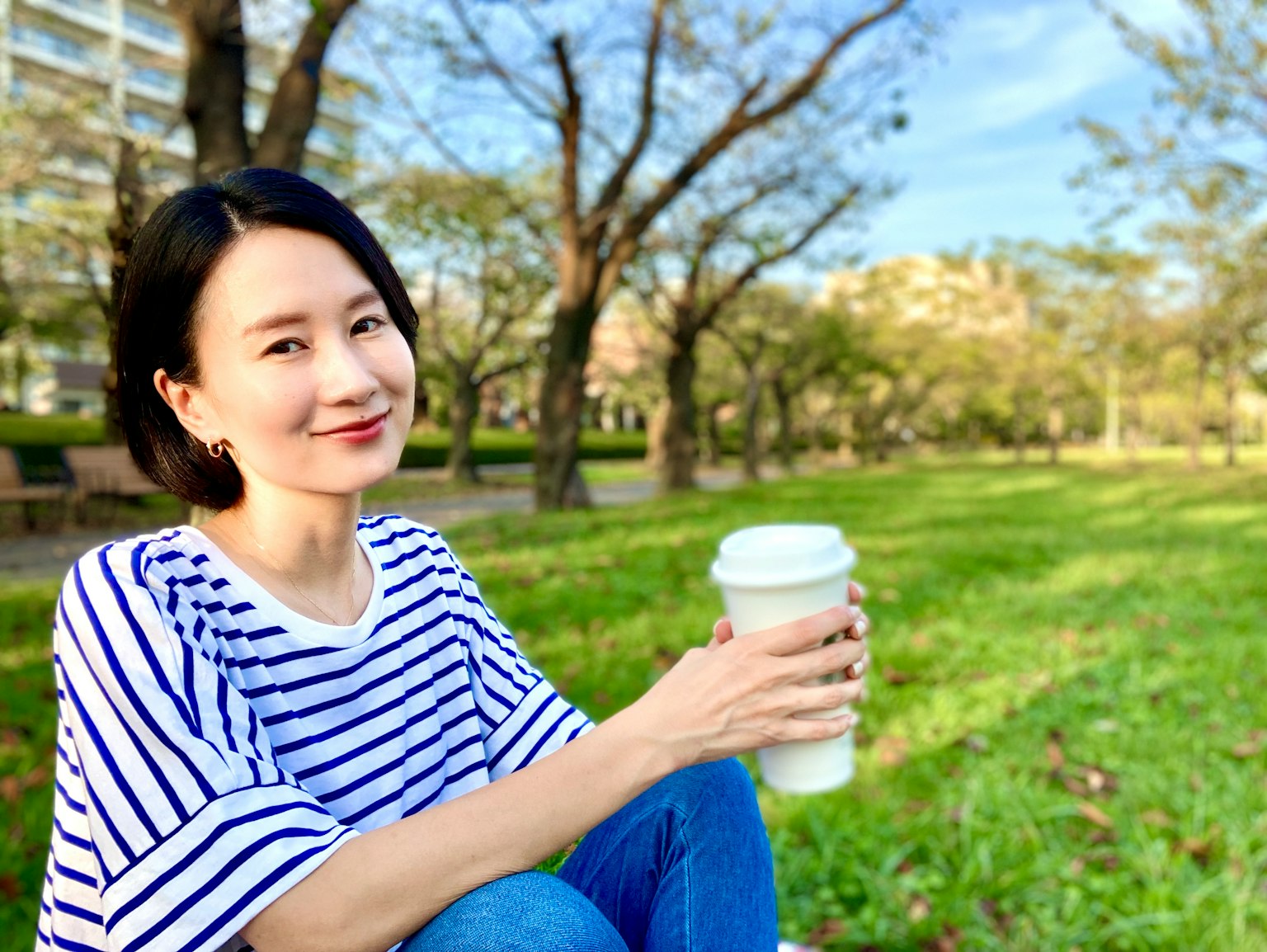 公园中拿着咖啡的女性肖像绿色草坪和树木作为背景