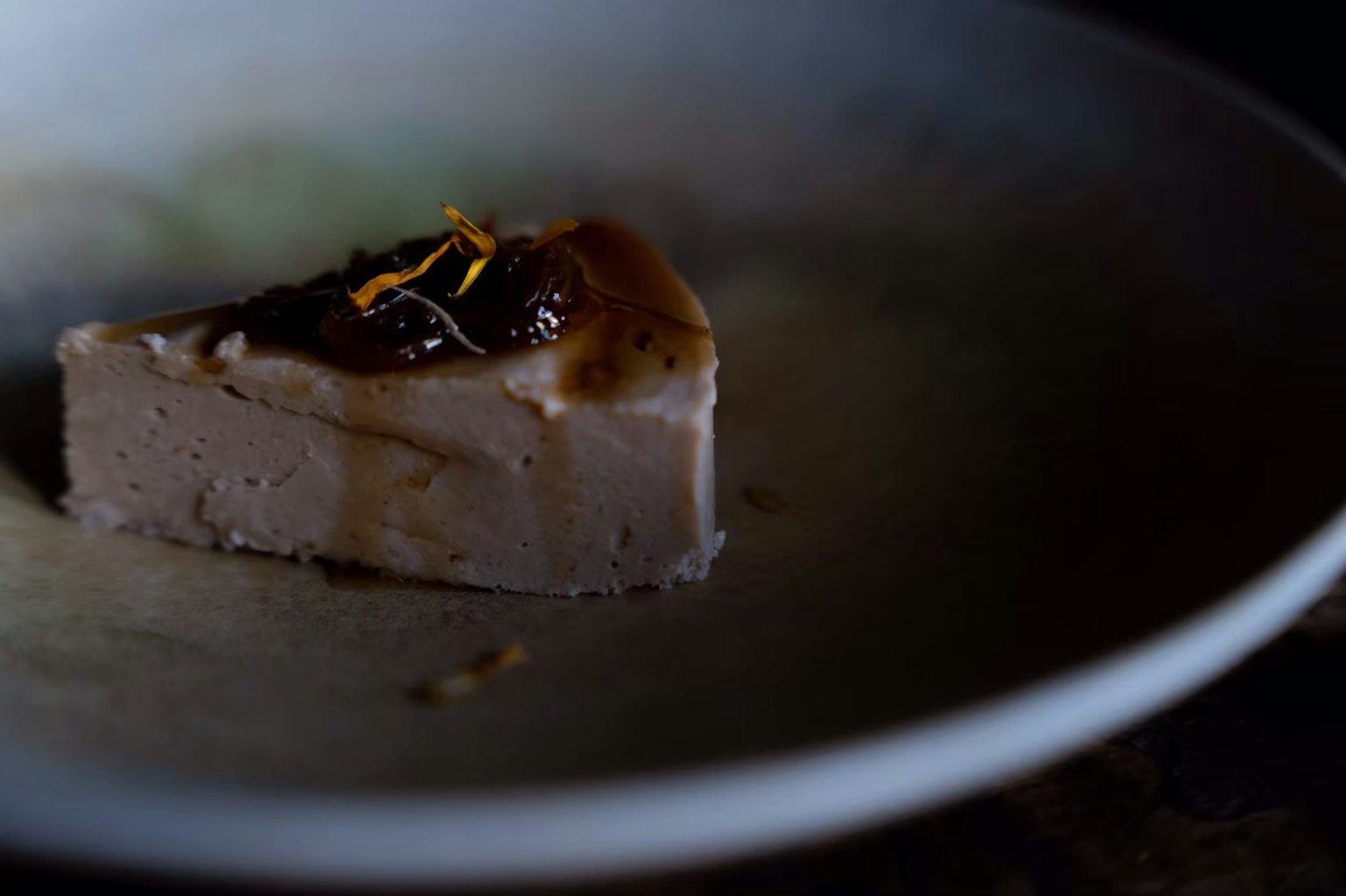 Una fetta di dessert su un piatto poco illuminato guarnita con scorza d'arancia e ganache