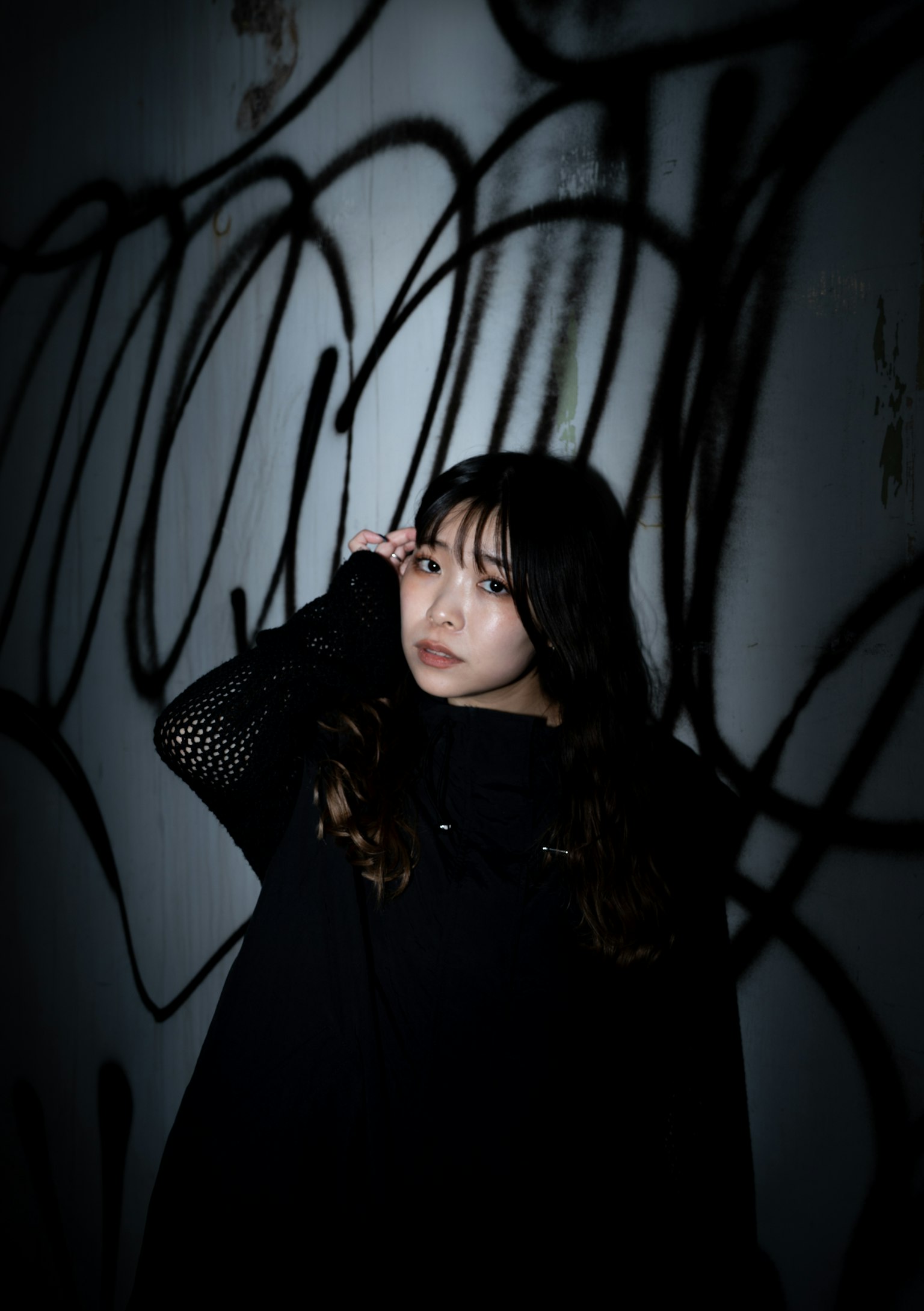 暗い背景に立つ女性のポートレート 黒い服を着ている 鮮やかなグラフィティの前でポーズをとる