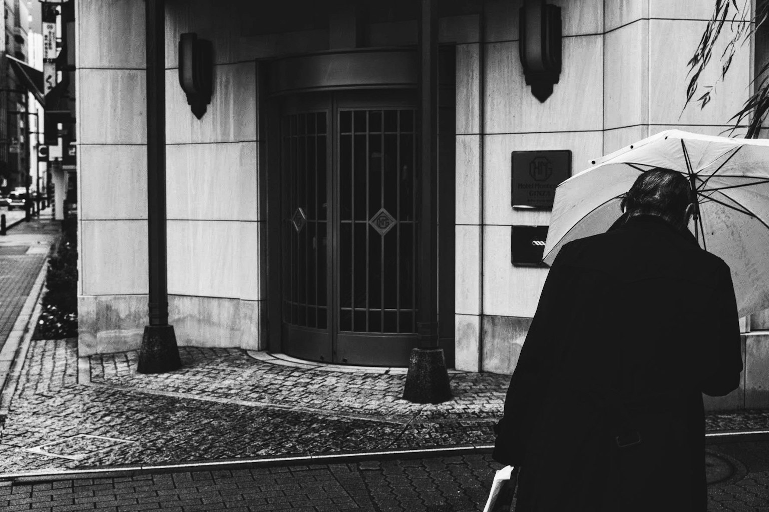 Una persona in un cappotto nero con un ombrello bianco all'angolo di una strada