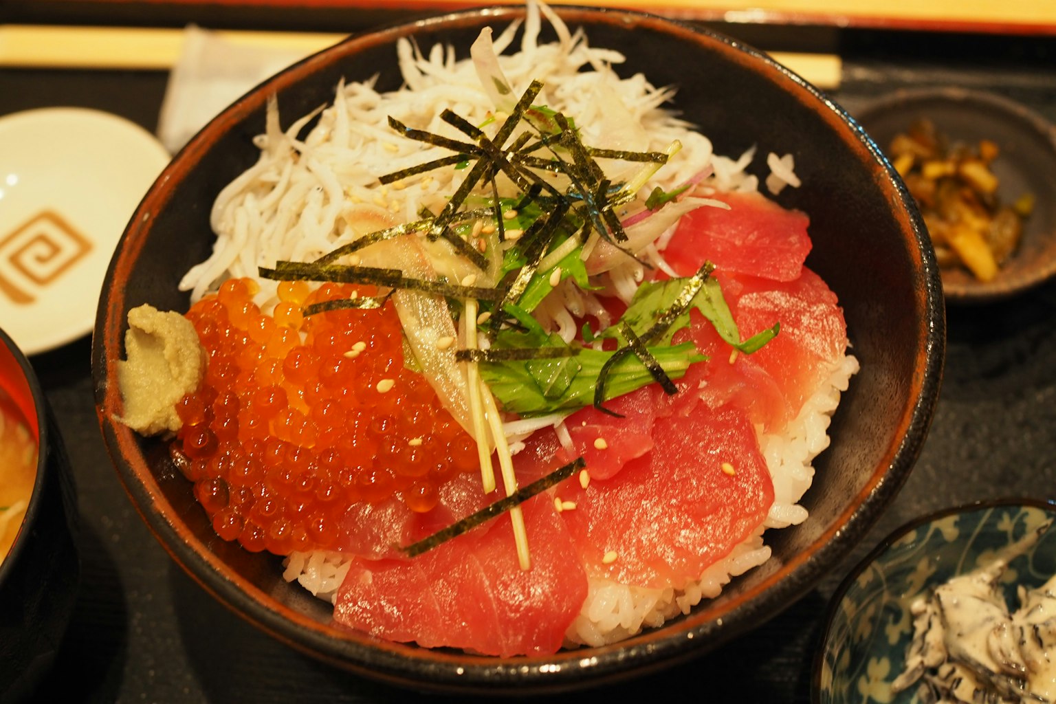 Ciotola di riso sushi guarnita con sashimi fresco tra cui tonno e uova di salmone decorata con alga e zenzero