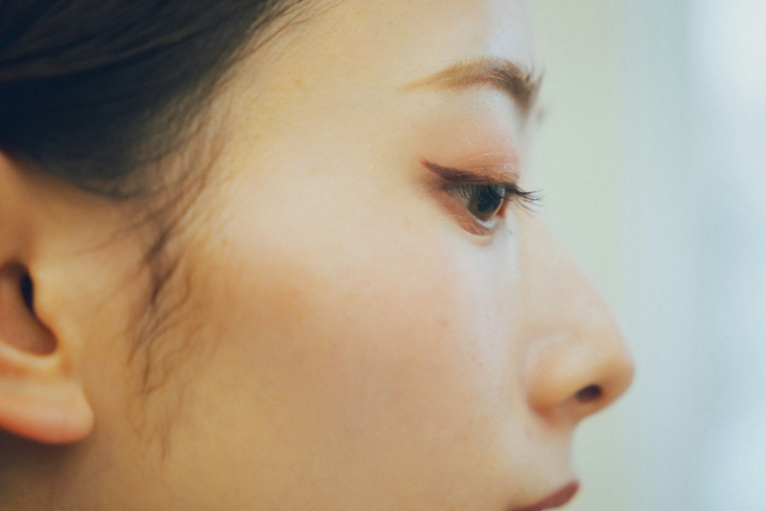 Nahaufnahme eines Frauenprofils mit weicher Haut und schönen Wimpern vor einem subtilen Hintergrund
